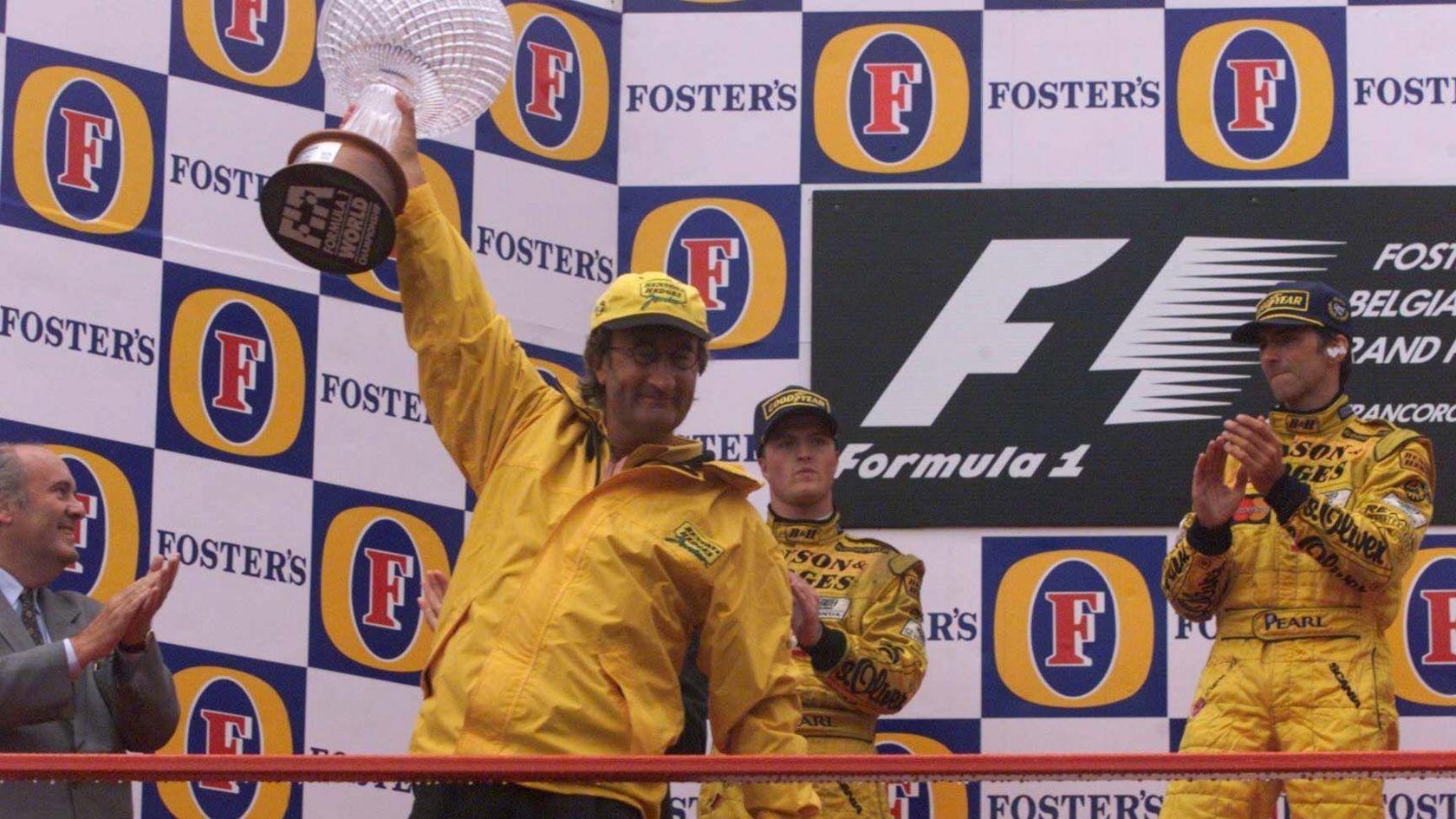 Eddie Jordan lifts the winning constructors trophy at the 1998 Belgian Grand Prix, with race winner Damon Hill and second-placed Ralf Schumacher behind him on the podium