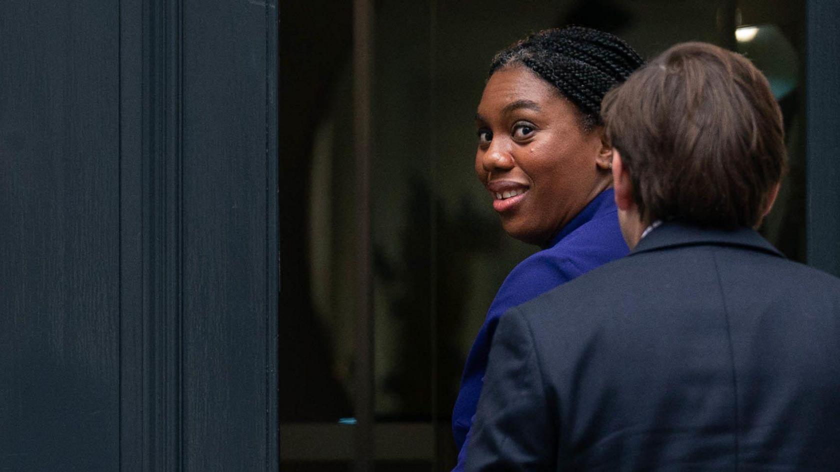 Kemi Badenoch walking into the entrance of a building, she is turning and looking over her shoulder to look towards the camera