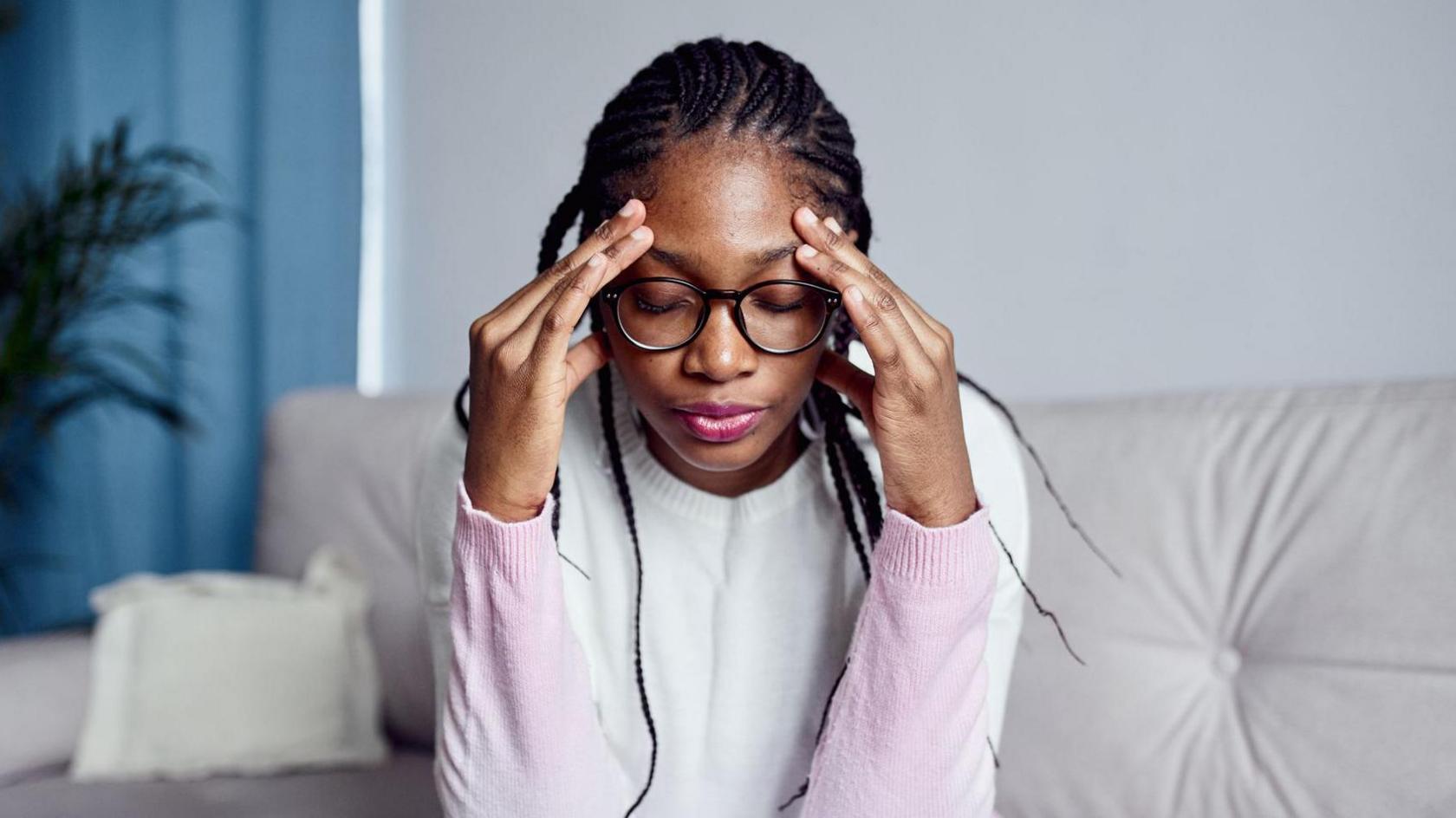 A young woman is sitting on the sofa at home with her head in her hands
