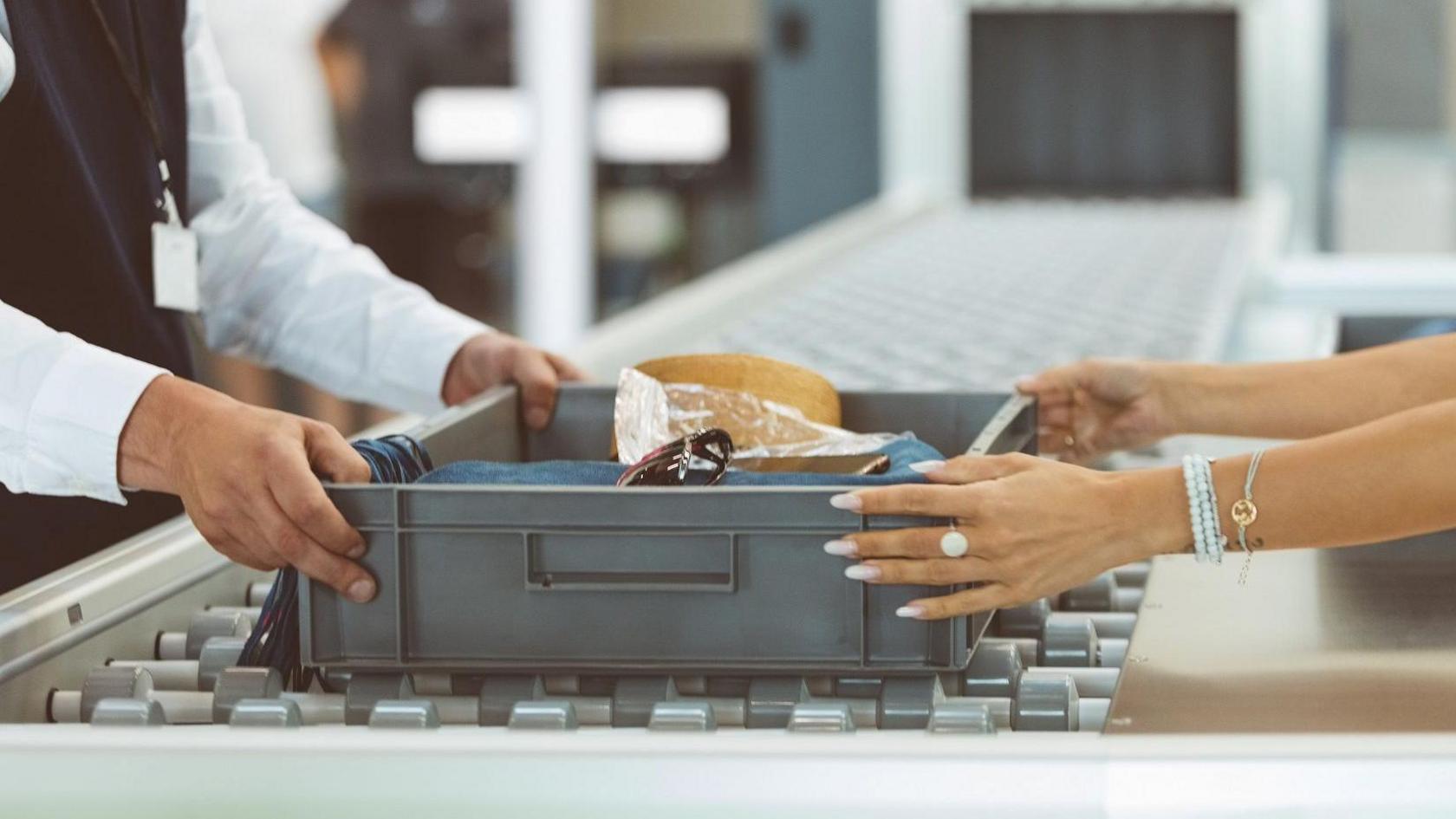 Security guard and passenger putting box through scanners