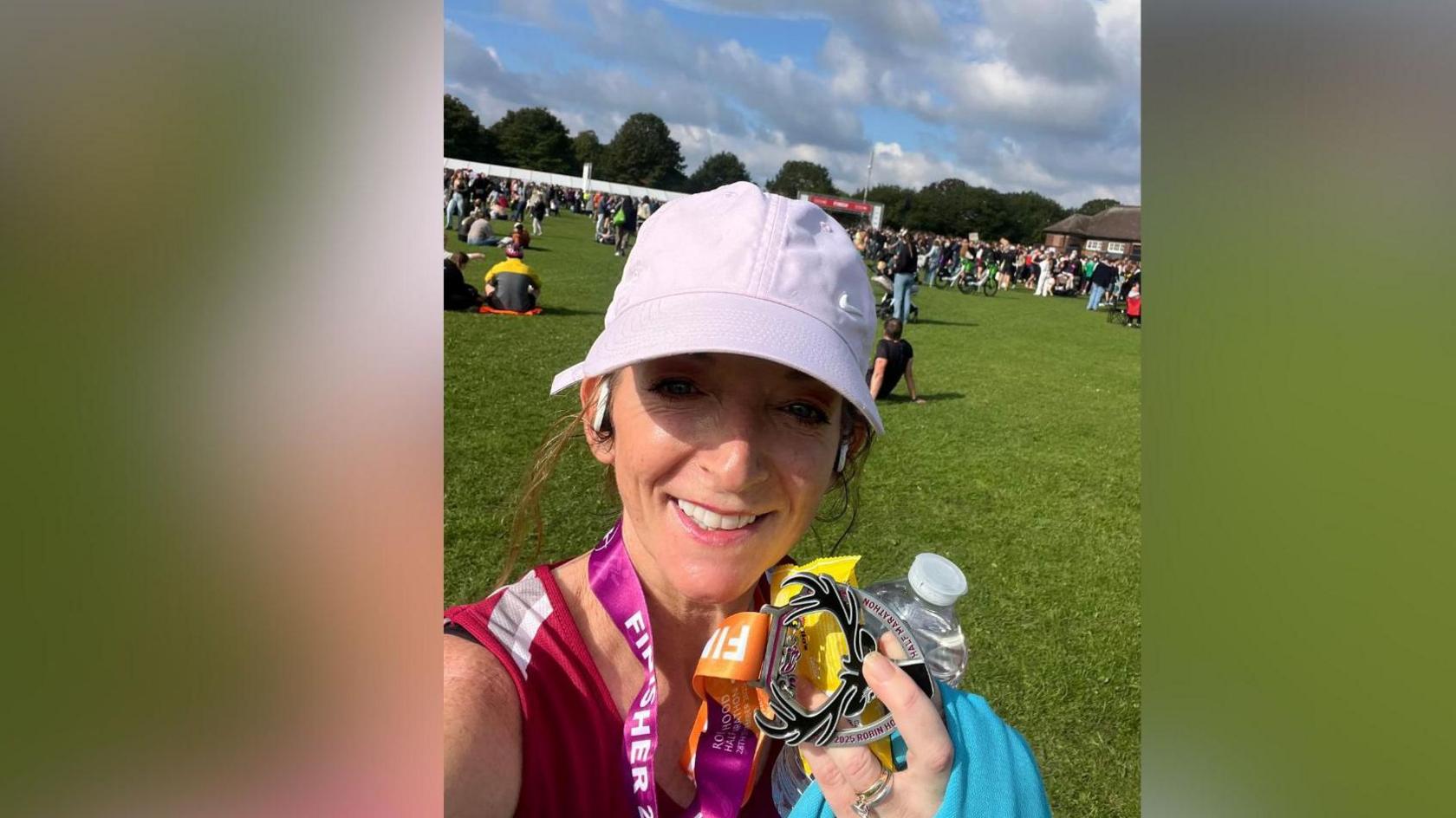 Sarah-Jane Hill holding a medal, with a cap on and a green field in the background which has people sat down there