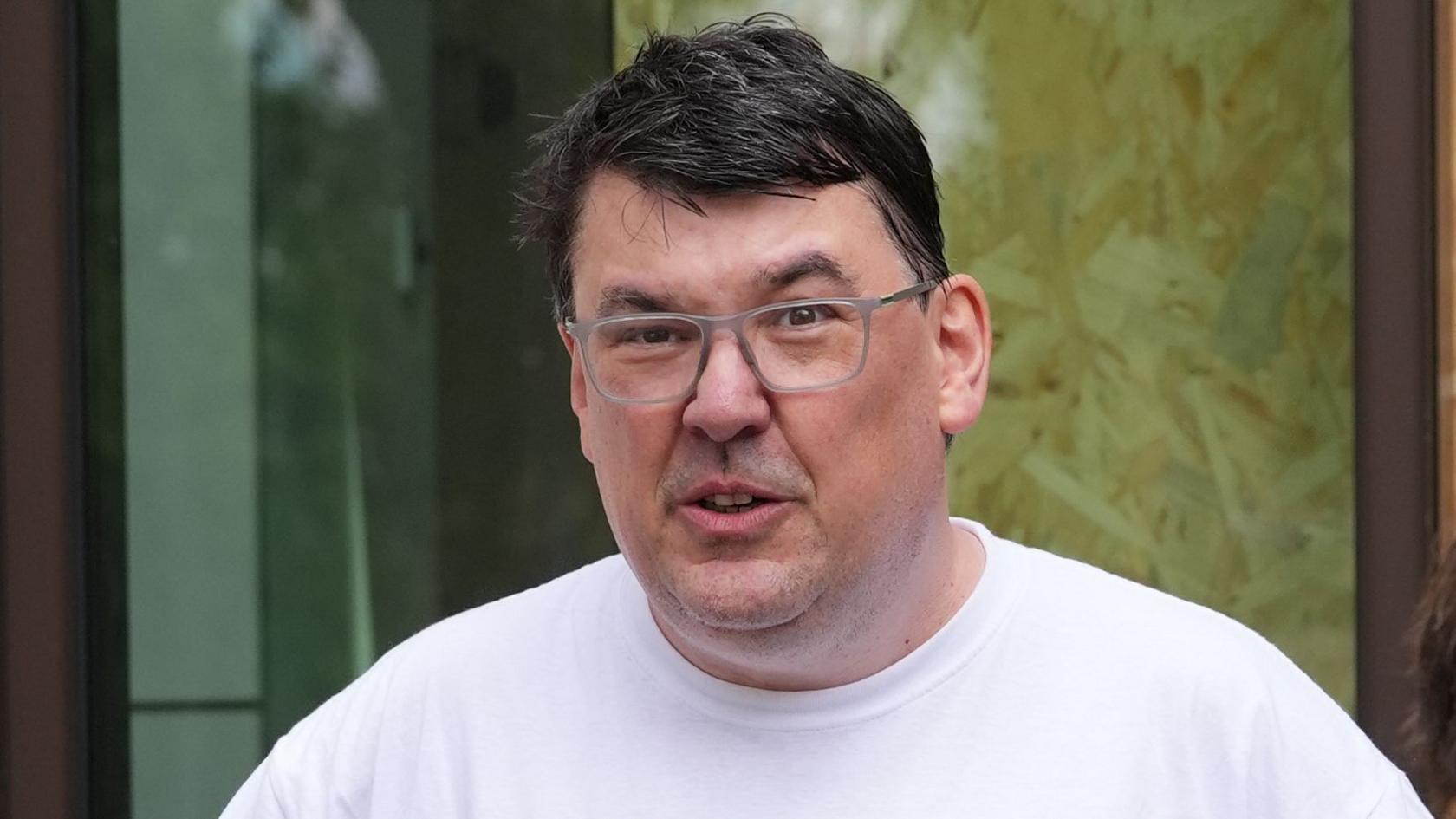 Linehan outside court in May, looking at the camera wearing glasses and a white T shirt.