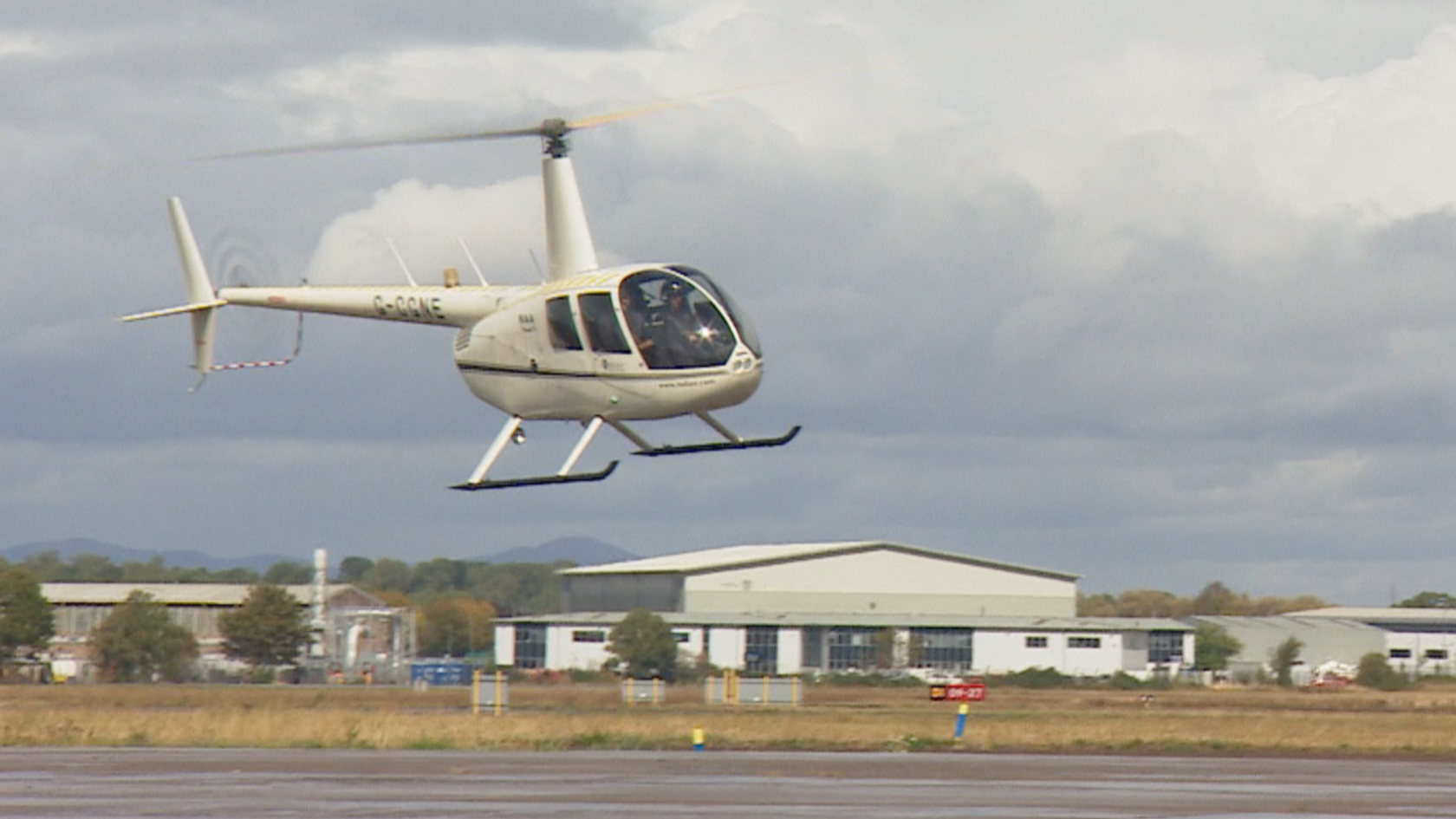 A small white helicopter hovering over a runway at Gloucestershire Airport.