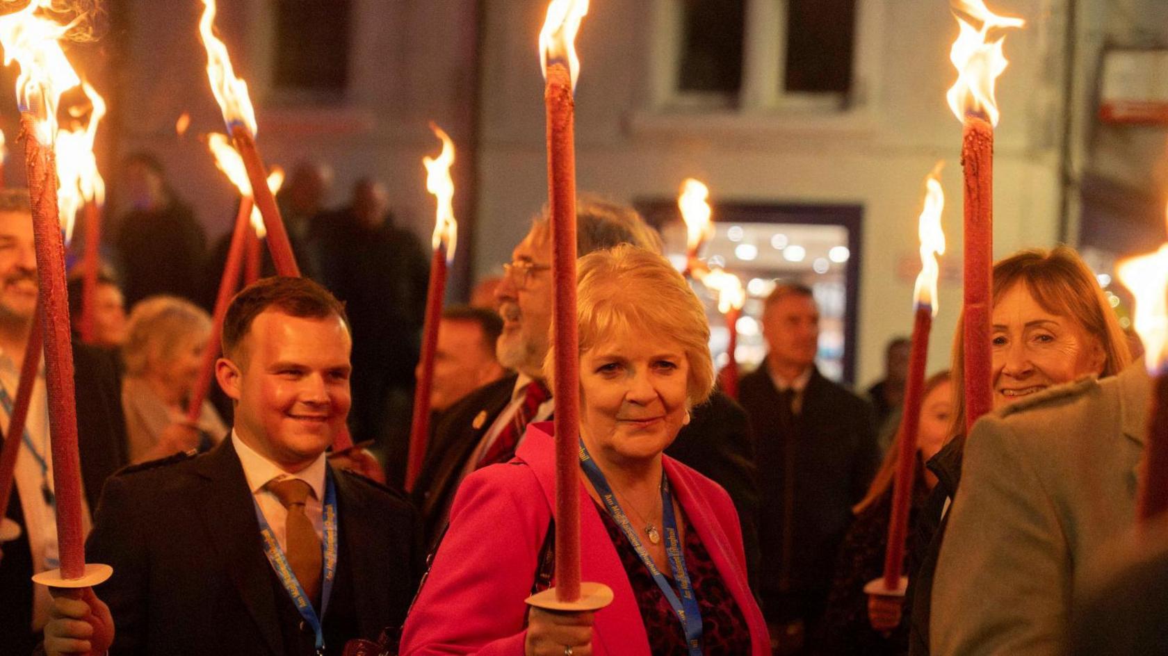 Peigi NicIllinnein agus lòchran laiste na làimh air caismeachd a' Mhòid