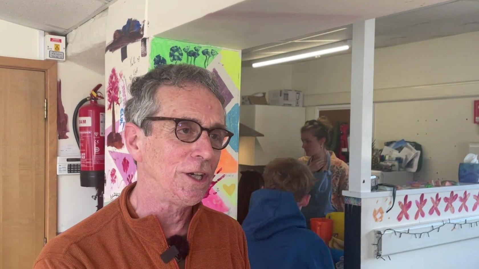 A man wearing glasses stands in a youth centre