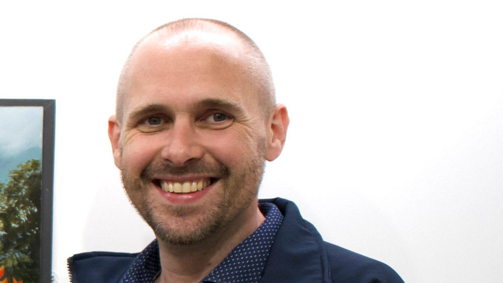 A man with a short beard and bald head. He is smilling at the camera.