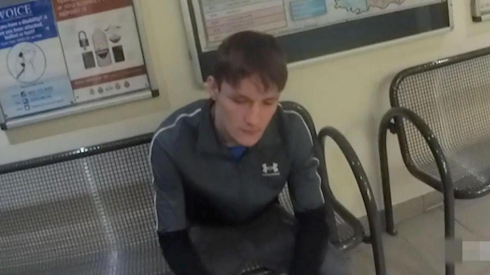 Hartle sitting on a chair in a police station wearing a tracksuit top