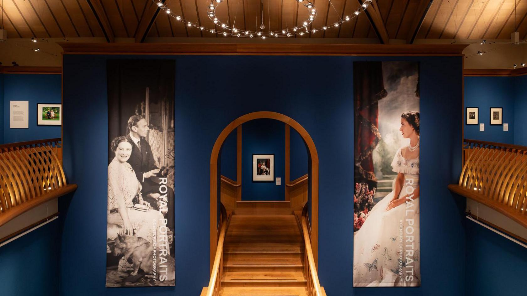 Wooden stairs lead up to a platform in the gallery. The walls are dark blue.