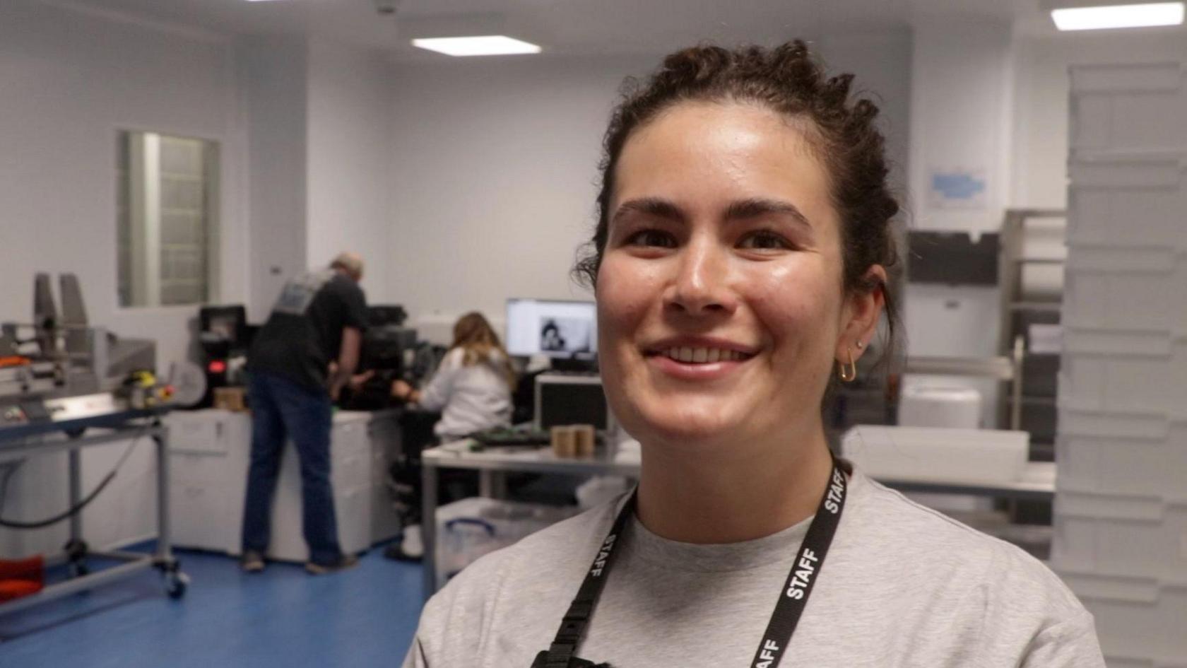 Tabitha Bonallie is standing in one of the laboratories. She has dark hair. People behind her are looking at a computer.