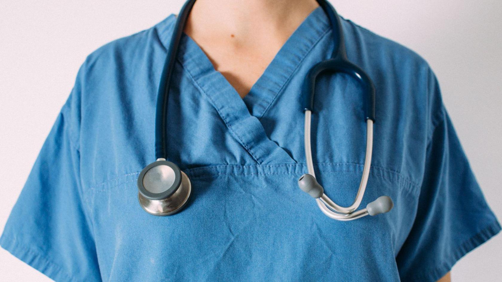 Close up of a female doctor's upper body in blue scrubs with a stethoscope around her neck