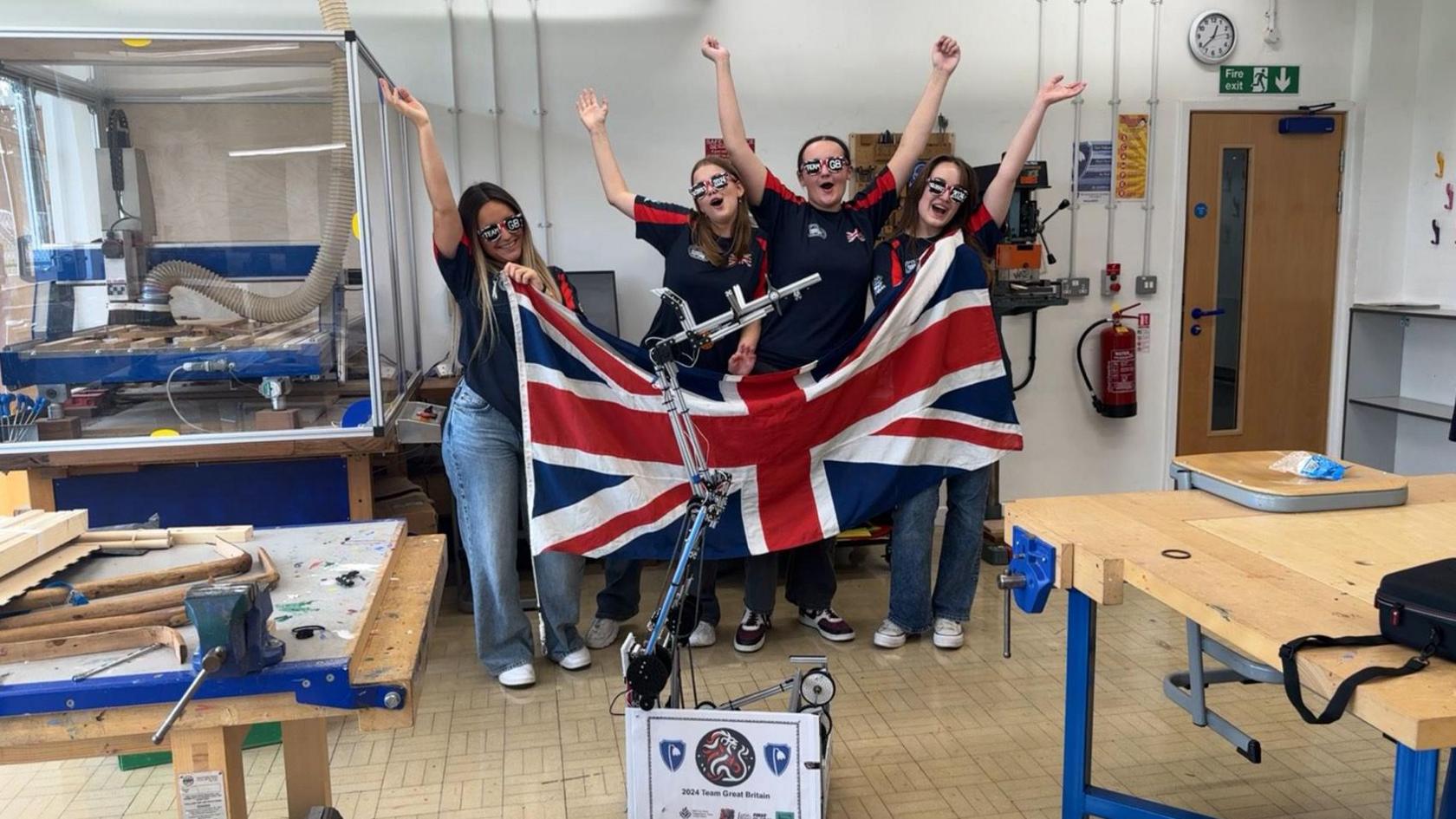 Four girls with a Union Jack flag stand in front of a robot