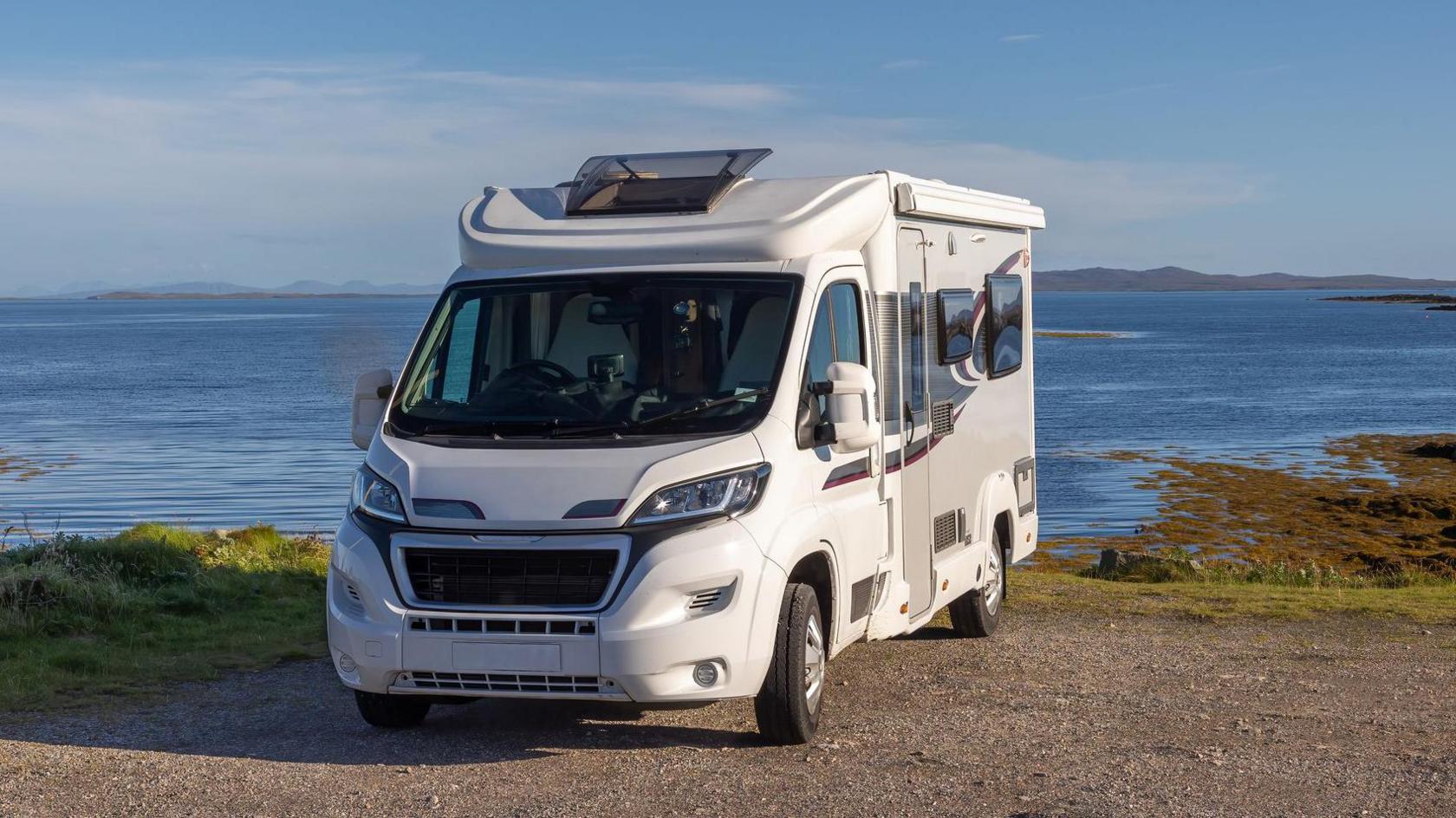 Front view of a white and grey motorhome parked with a view overlooking the sea.