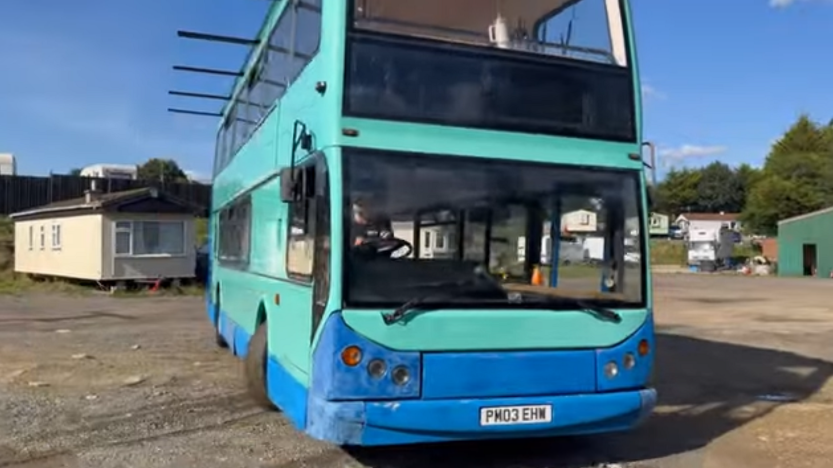 An ancient blue bus with a hole in the roof and panelling falling off the top. 