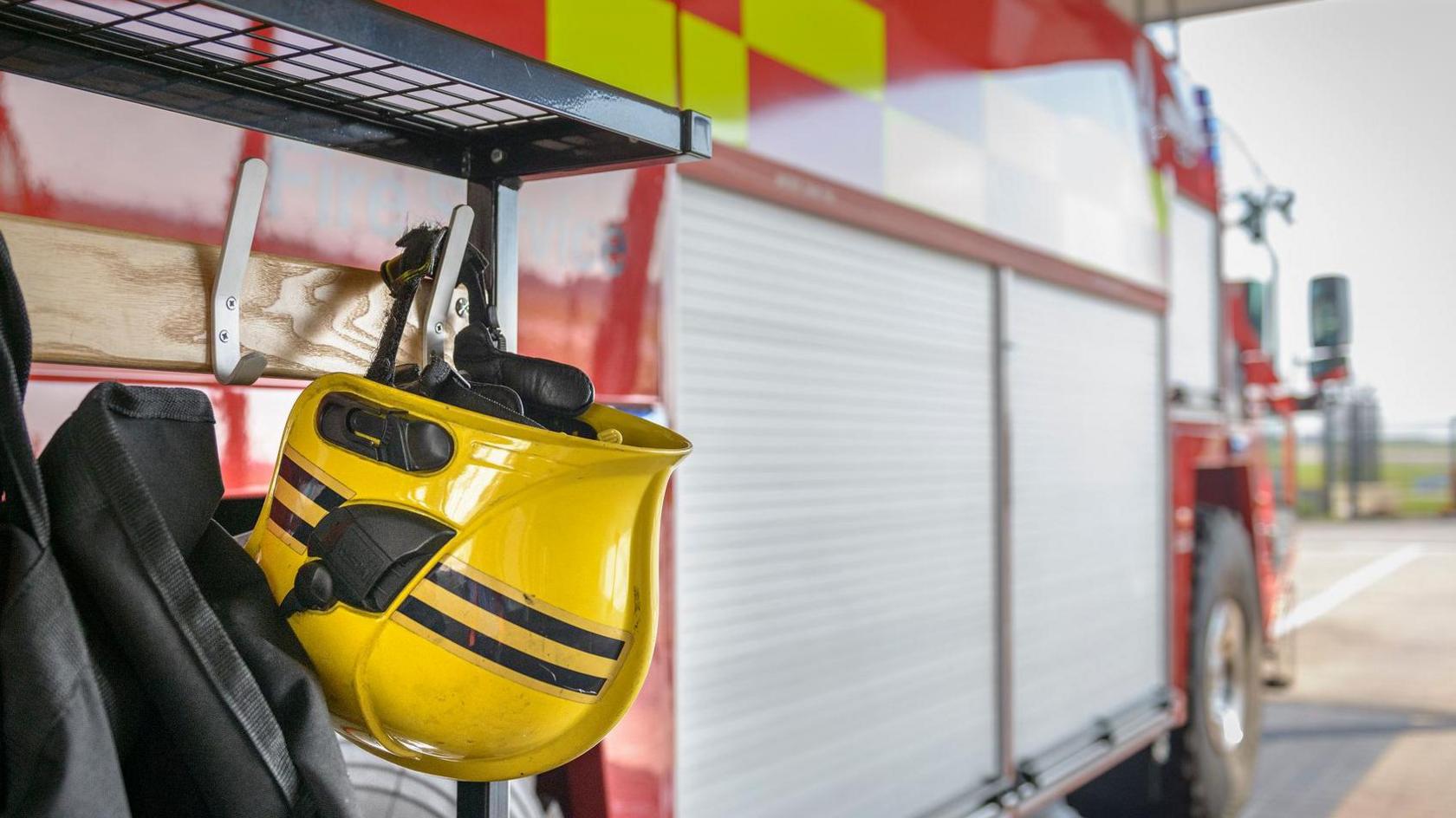 A firefighter's helmet in the foreground hangs from the side of a red and silver fire engine.