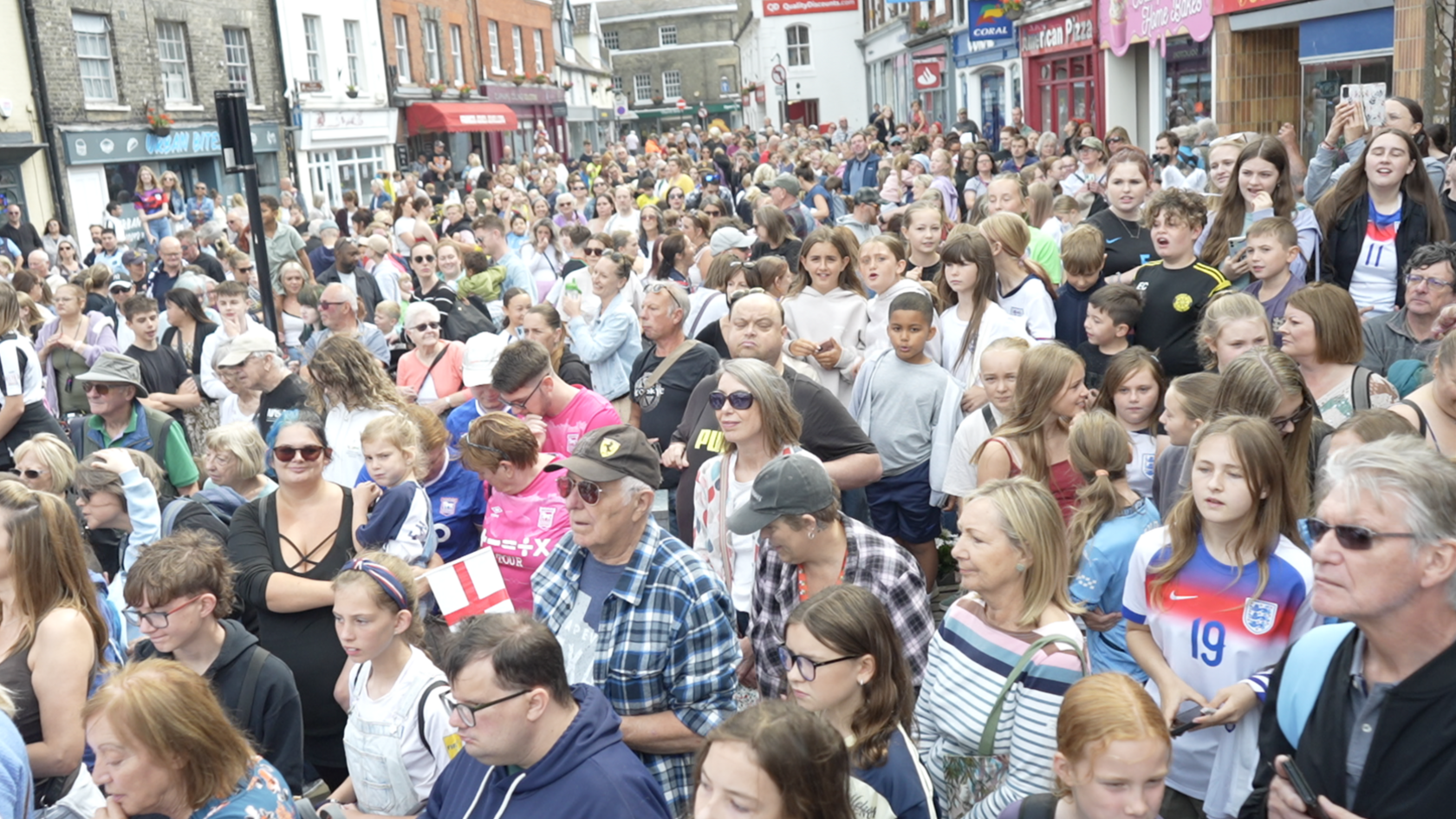 A crowd of hundreds of people fill a town centre road.