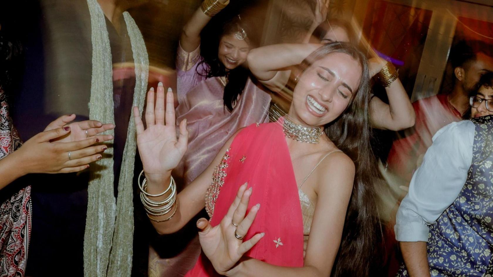 Young women, wearing colourful Indian outfits, dance at a party