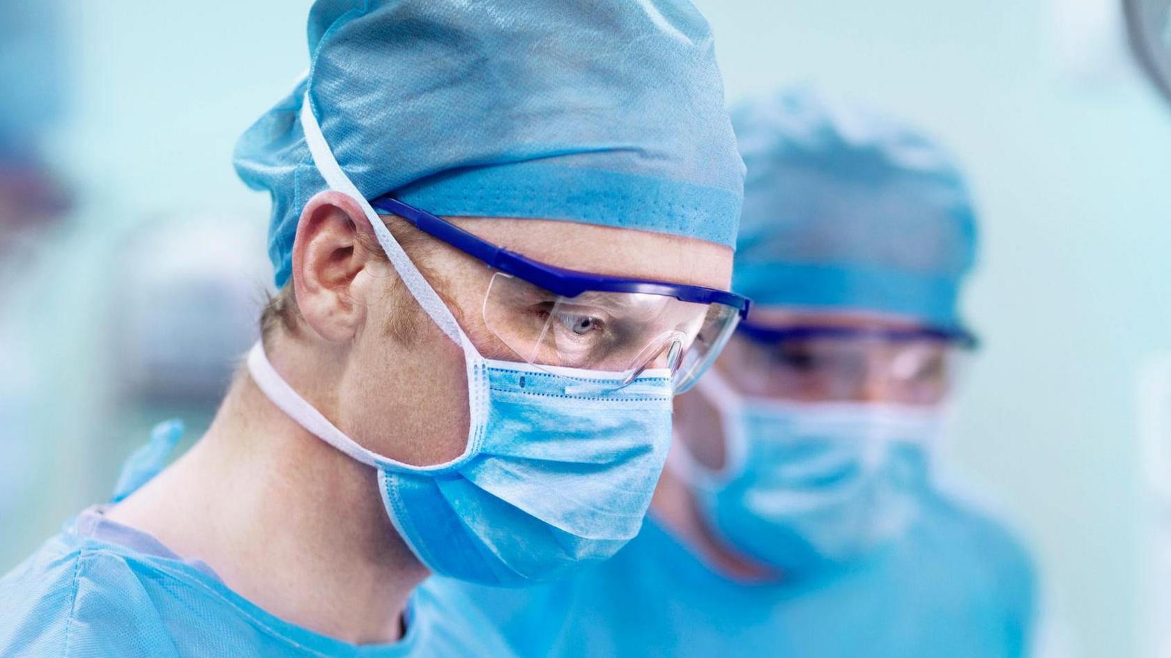 Two doctors dressed in scrubs, masks and glasses looking down.