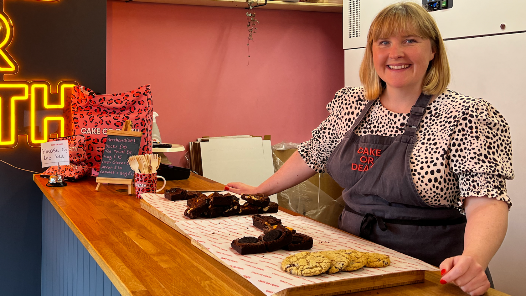 Katie Cross is wearing an apron, stood at a counter top with baked goods on in front of her.