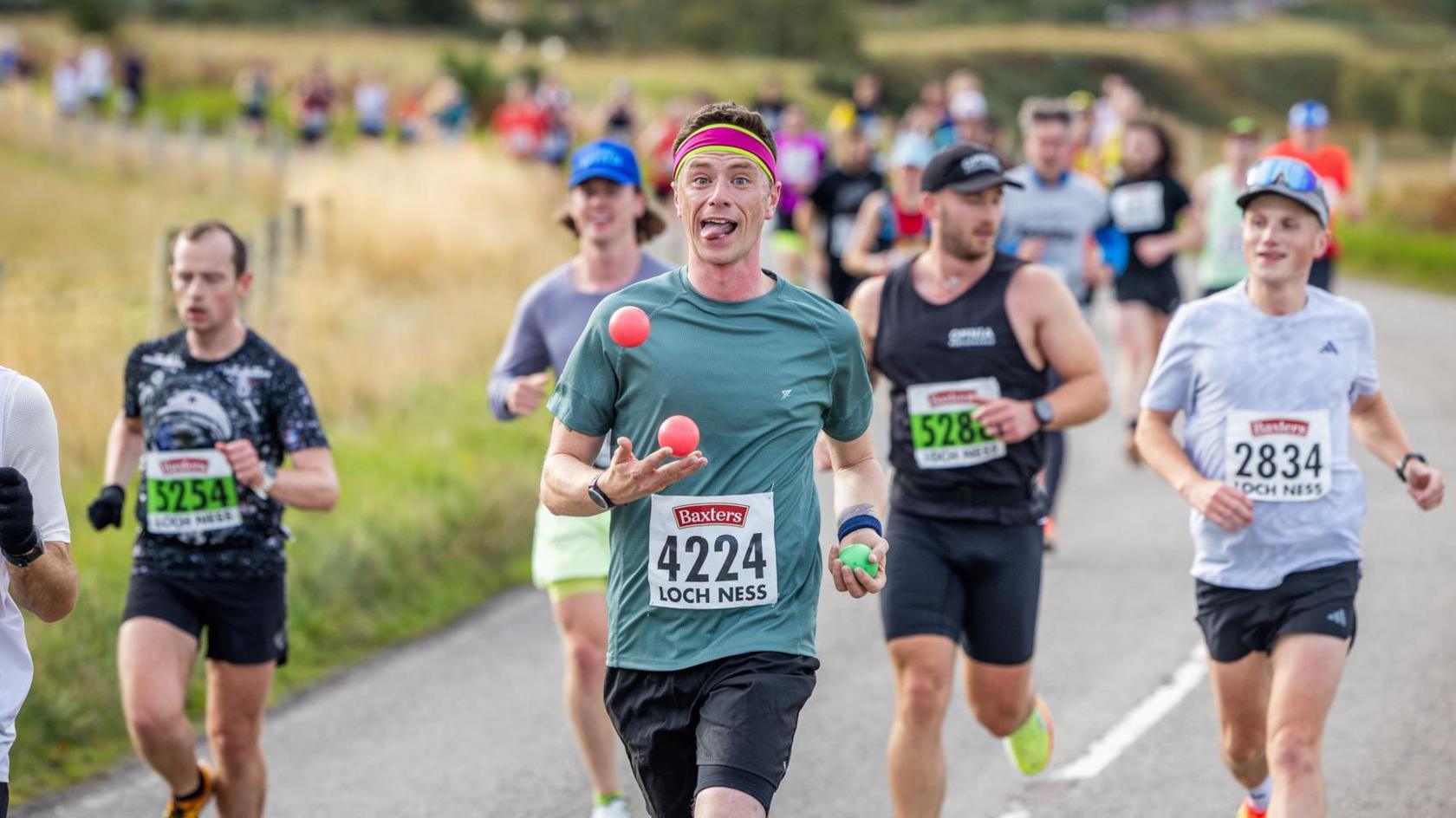 A runner juggles red and green balls as he runs in front of other runners