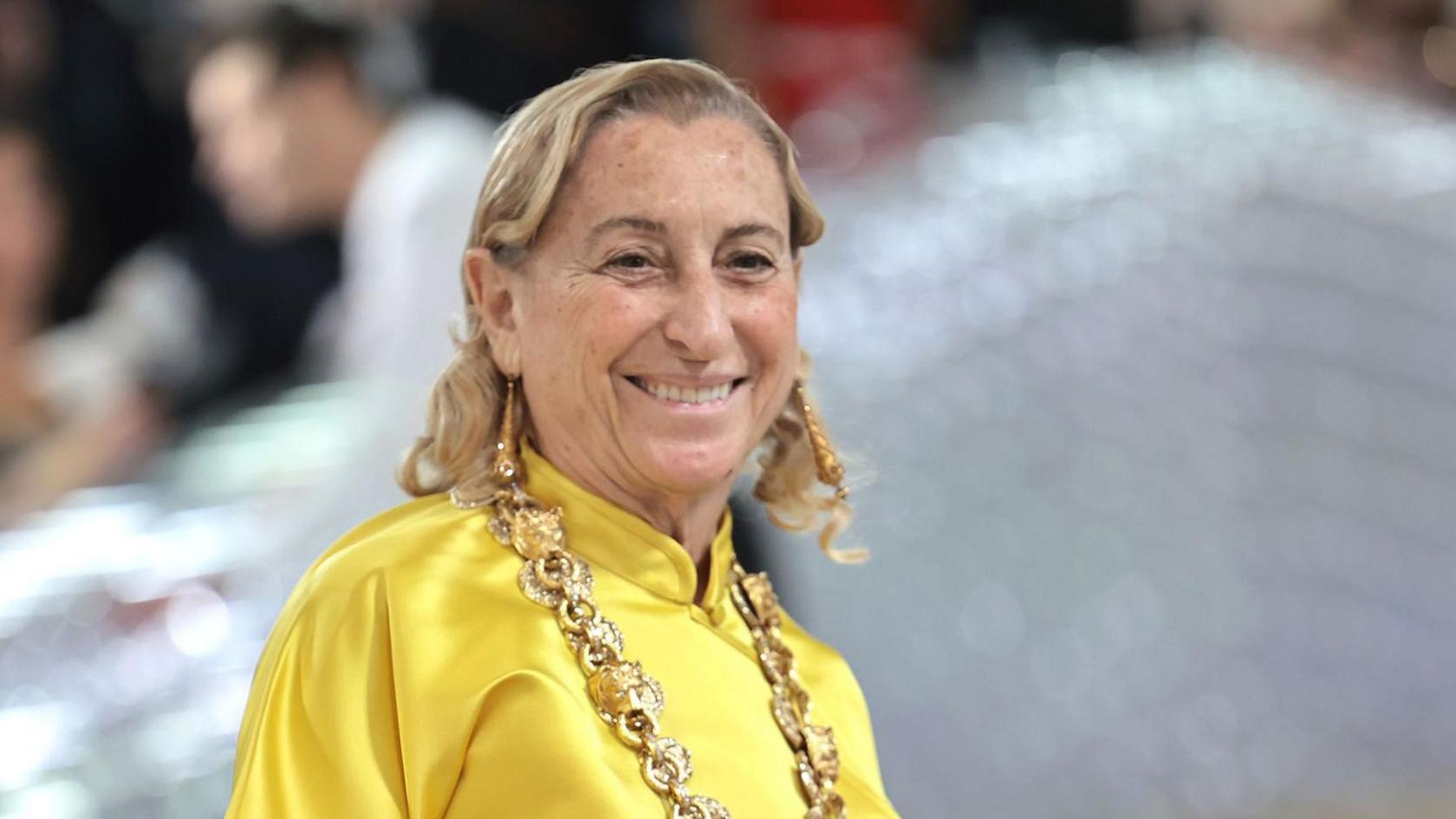 A smiling Miuccia Prada wears a yellow satin top and large gold chain at the Met gala