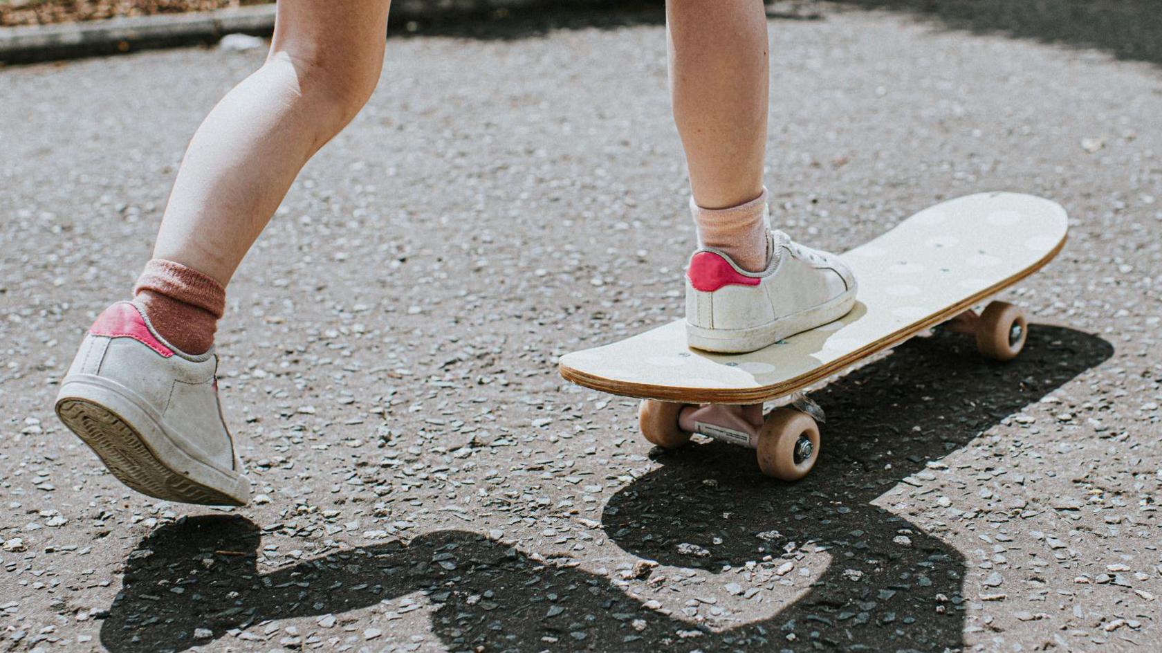A stock image of a child on a skateboard. The child is wearing white and pink trainers and mismatched pink socks. 
