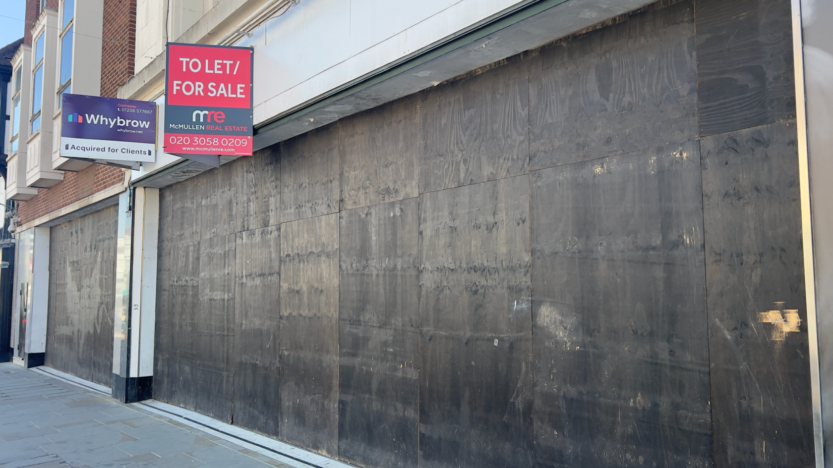 A boarded up shop in Colchester. Its former windows have been blocked up by planks of wood, which have been painted black.