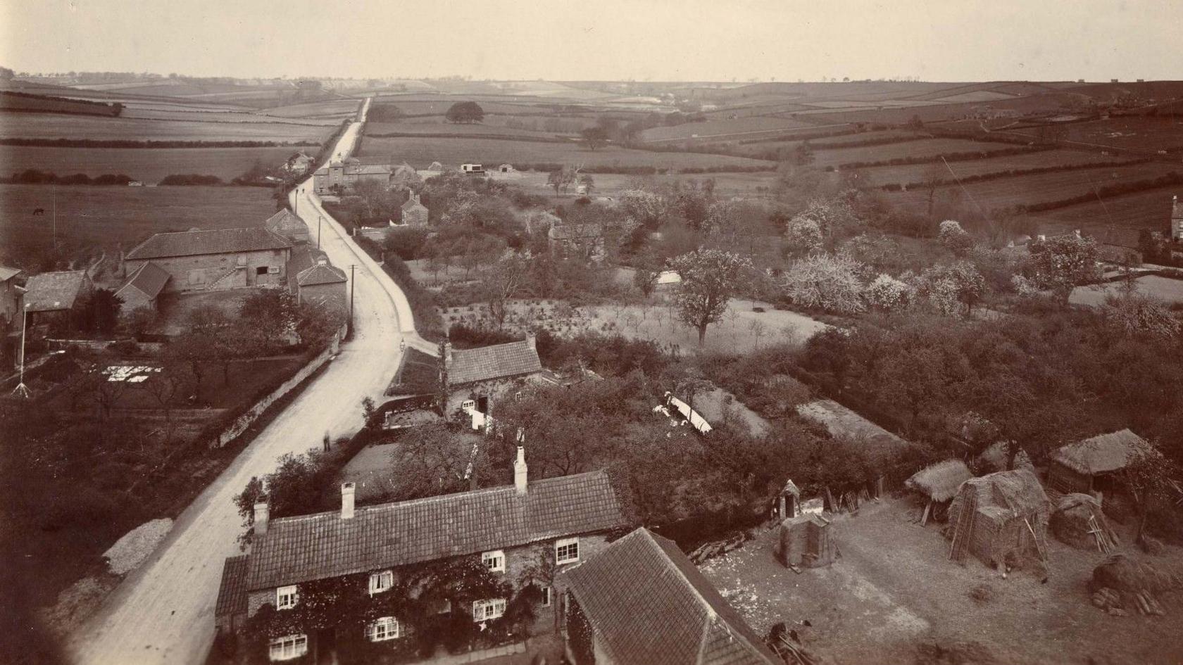 Old image of winding road with buildings in foreground.