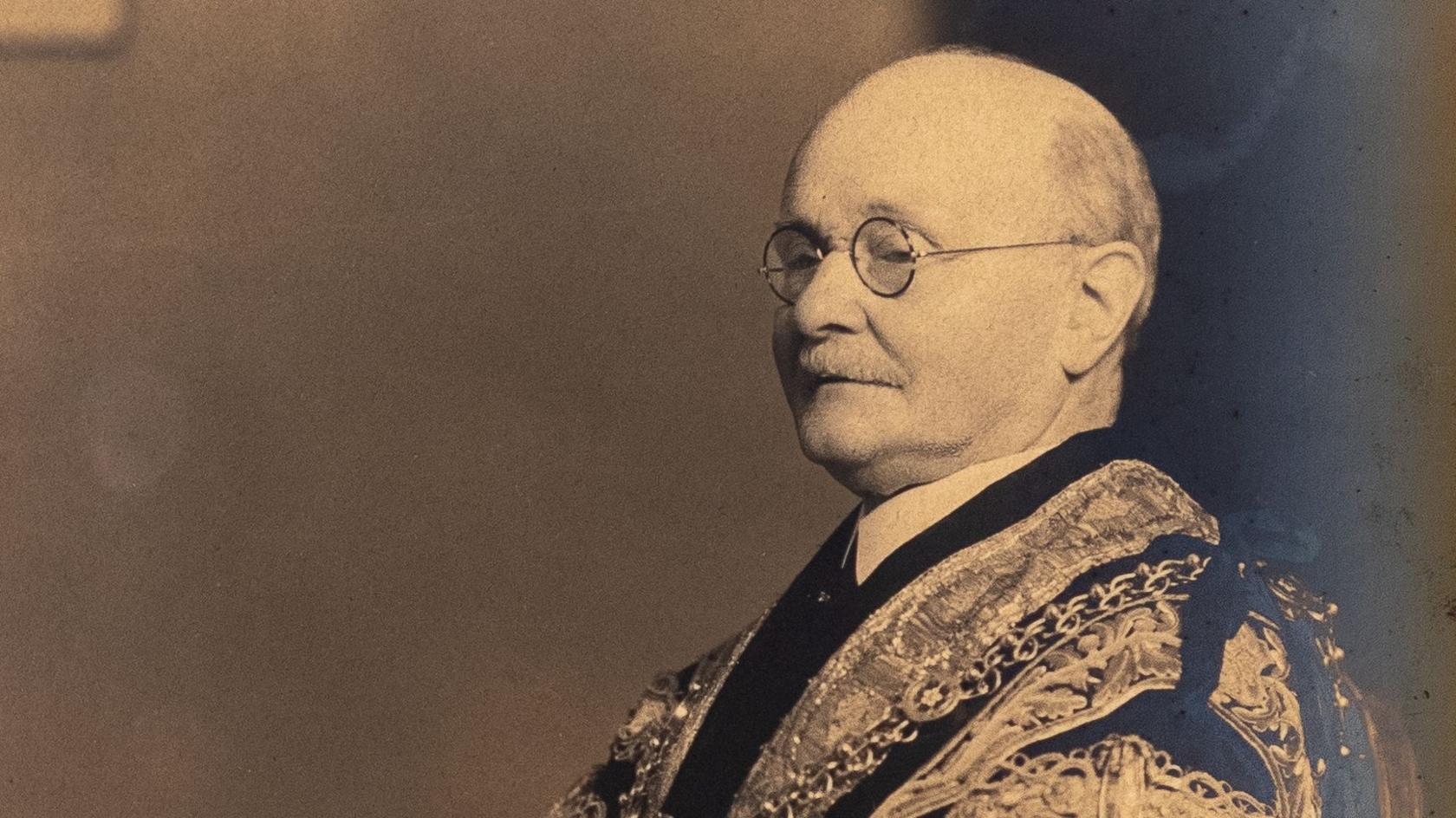 A sepia toned photograph of a bal man with glasses and moustache wearing ceremonial robes.