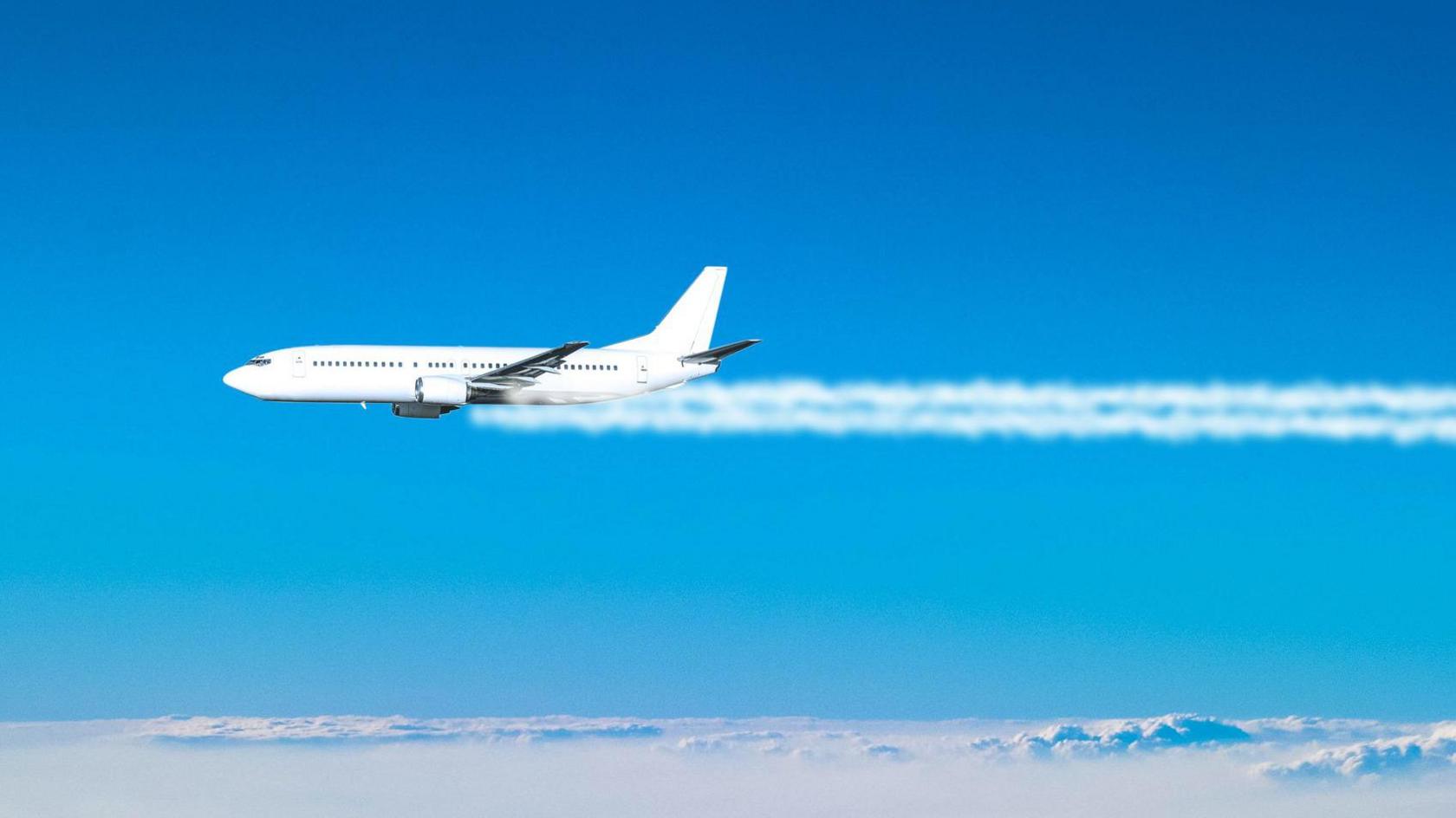 A jet plane flies across the blue sky, with white contrails coming from its engines