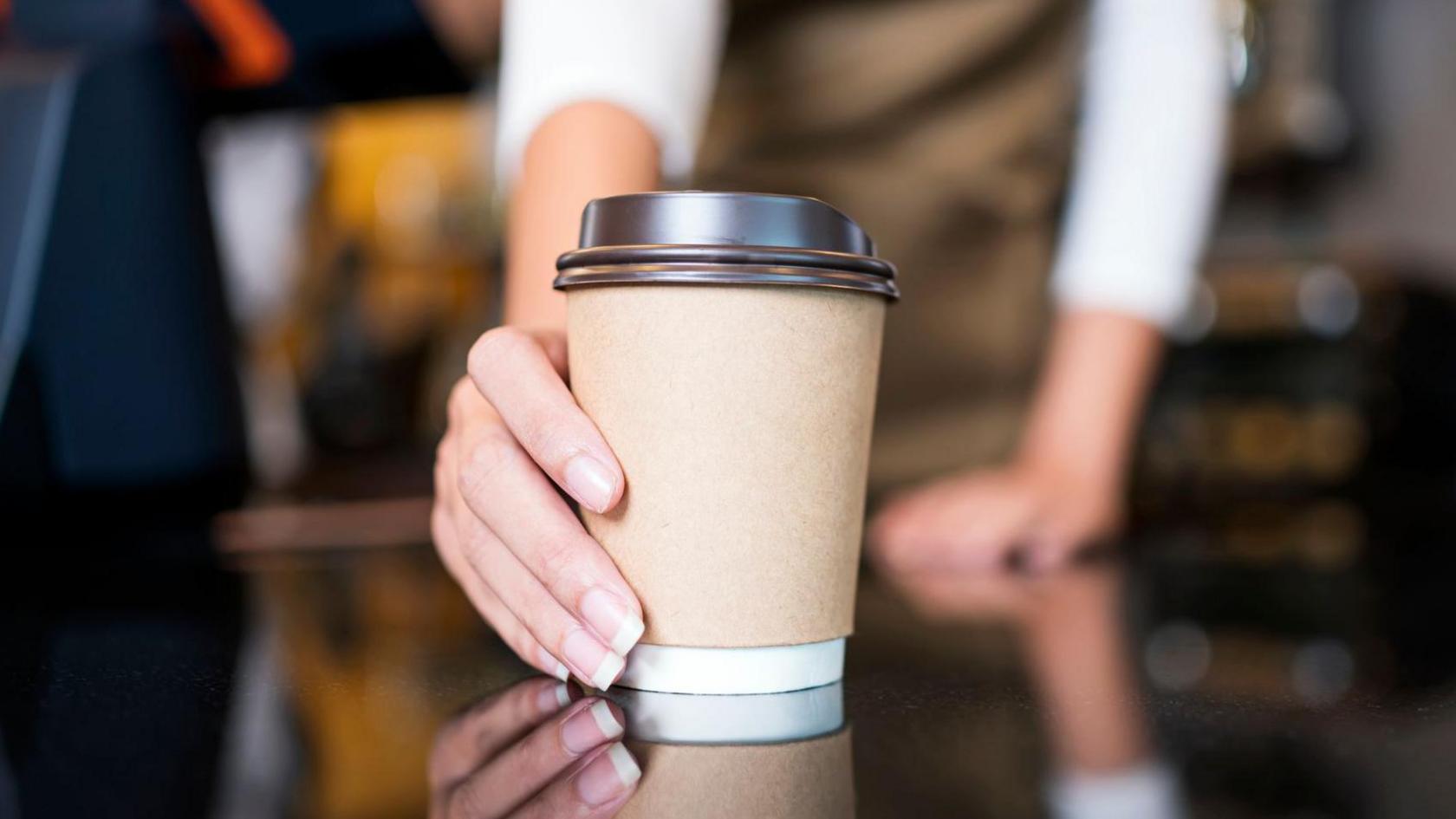 Woman's hand holding a brown paper cup with black lid