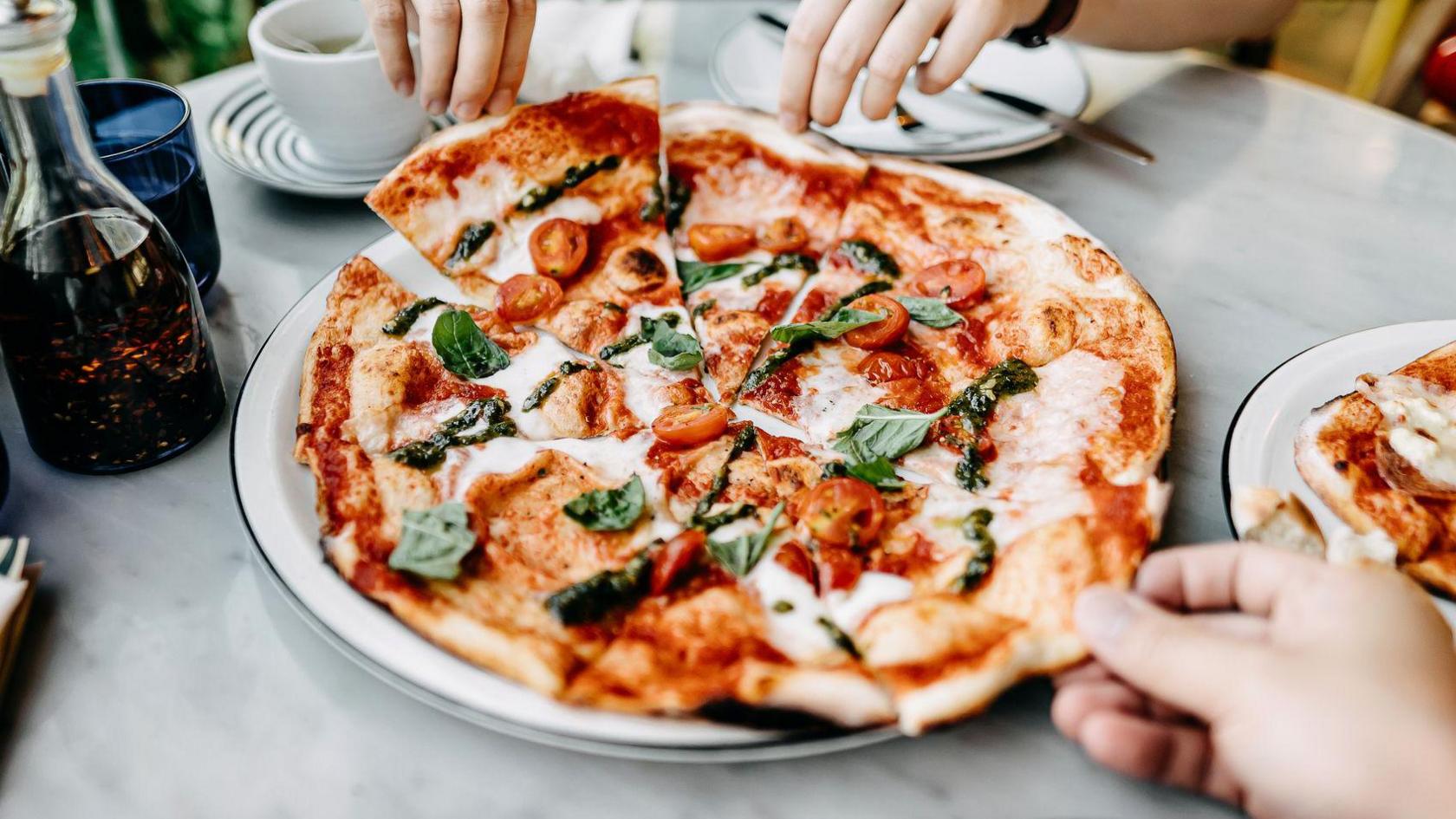 A pizza cut into slices, with two people taking a slice. 