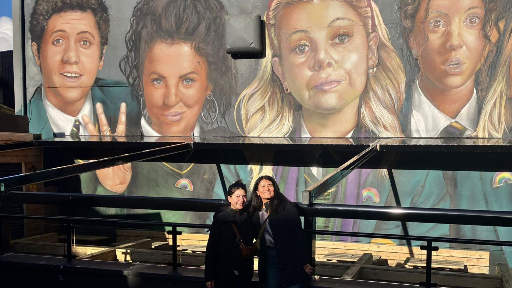 Constanza Jorquera and her sister, Sofia Jorquera, dressed in black standing in front of the mural