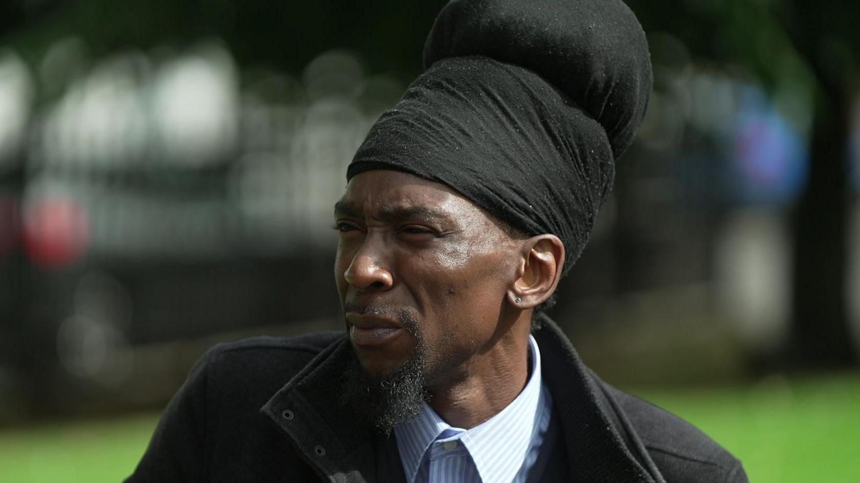 Takura Makoni wearing a blue and white striped shirt and black coat. 