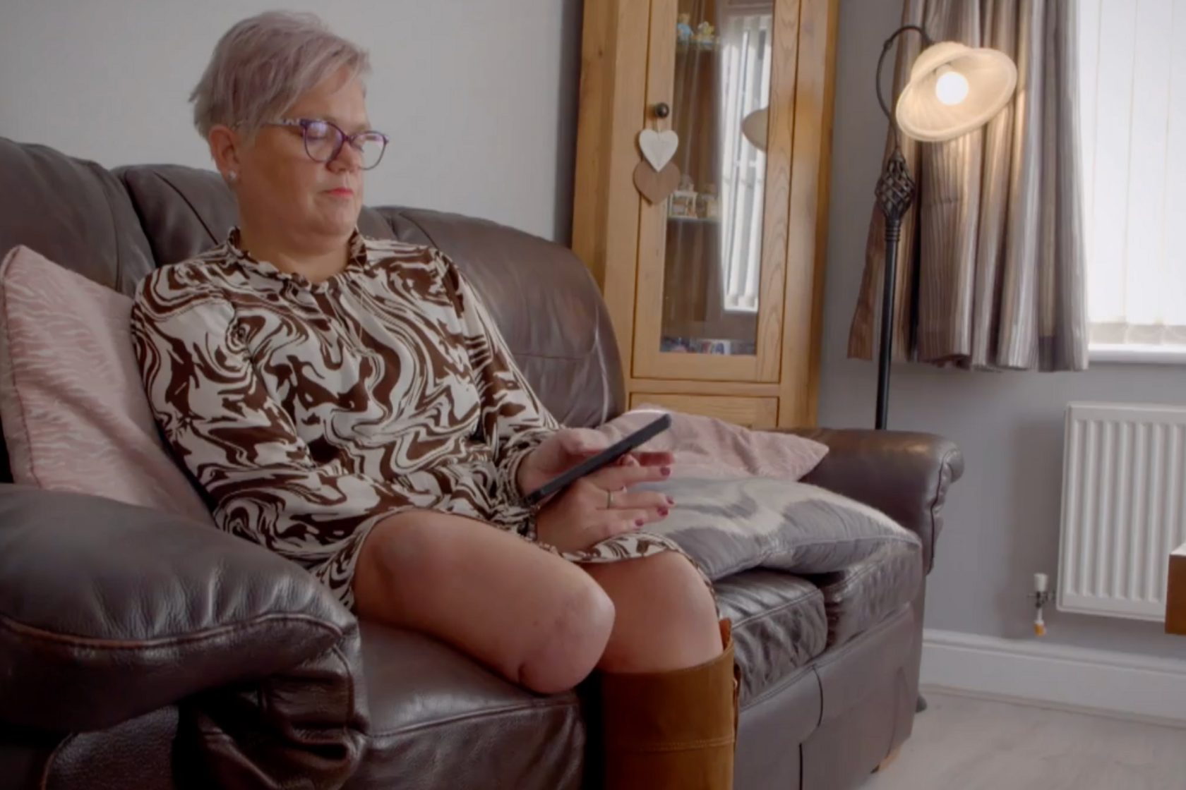Jo on her sofa dealing with online orders via her phone. She is white, has light purple hair and her missing limb is clearly visible