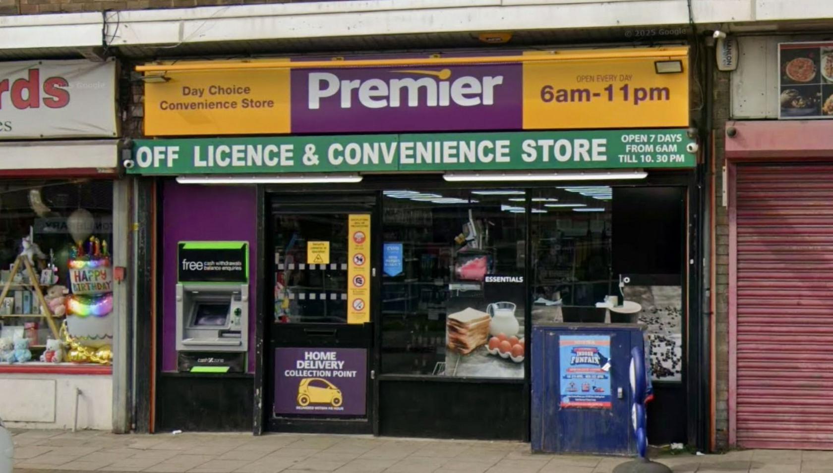 The exterior of a Premier Stores shop in Moreton. It has a cash machine next to the door and a blue junction box with some fly-posting on it. 