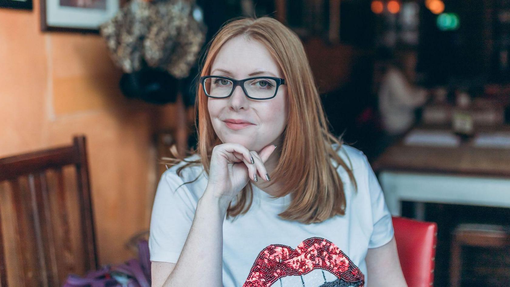 Leah Steele smiles, sitting in cafe wearing a t shirt