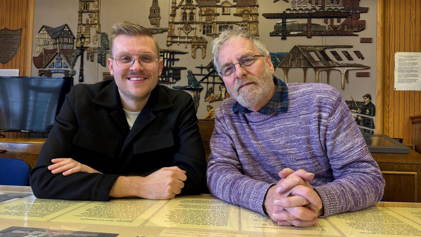 Andy Vallentine has short blonde hair styled in a quiff. He is wearing glasses and a black jacket. Next to him is Mark Hignett. He has short grey hair and glasses, and is wearing a purple jumper.