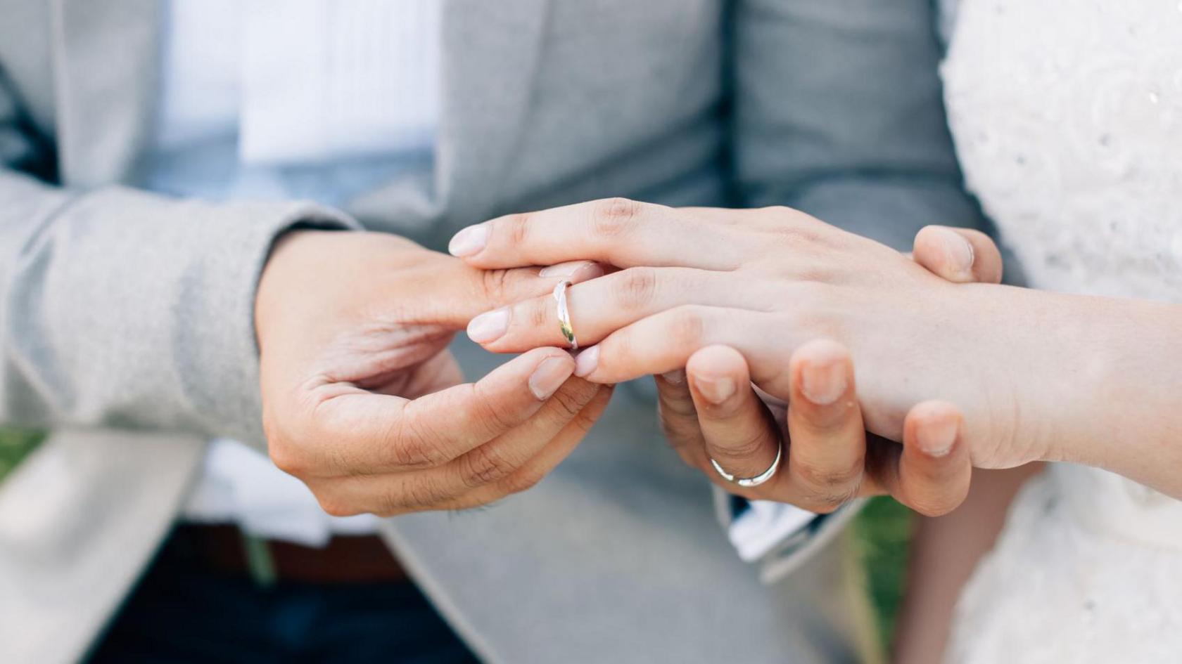 A groom placing a wedding ring on the bride's finger.