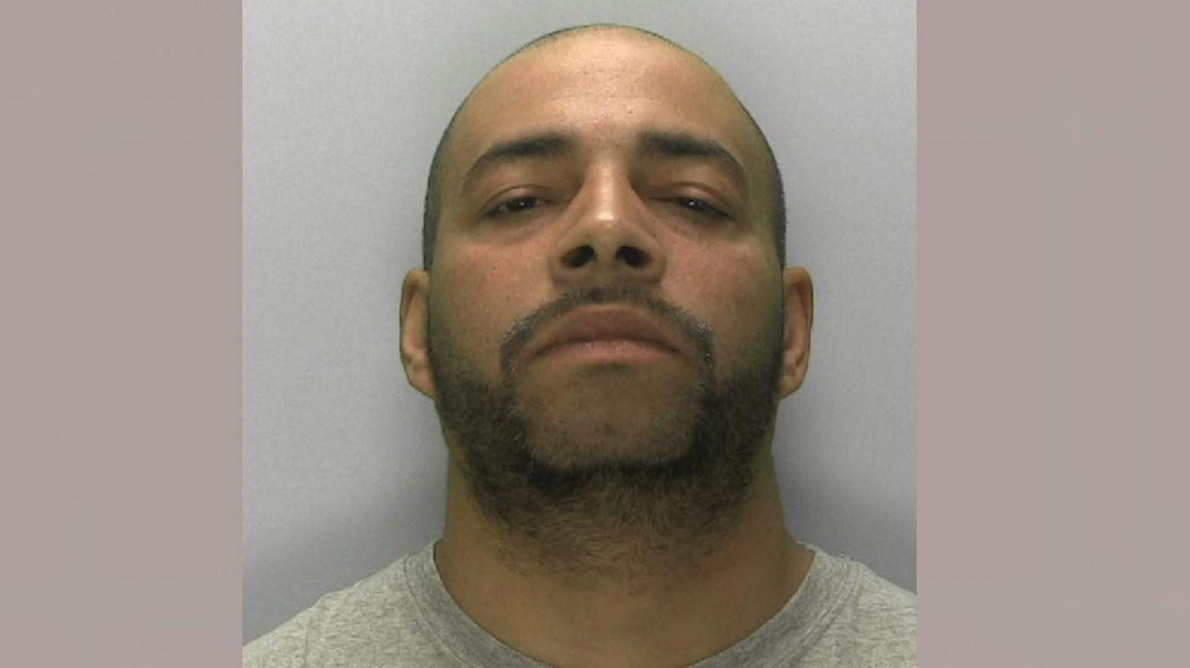 Darren Atkins looking at the camera in a police mugshot. He has a light covering of stubble and a shaved head. He is wearing a grey sweatshirt