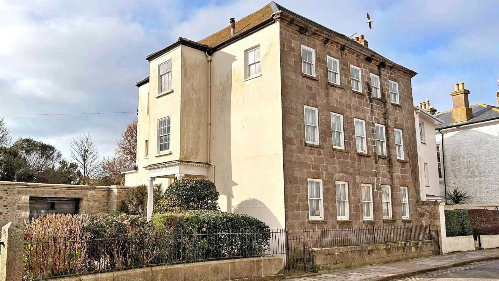 A three-storey town house with a granite brick front and cream side wall, photographed on a sunny day.