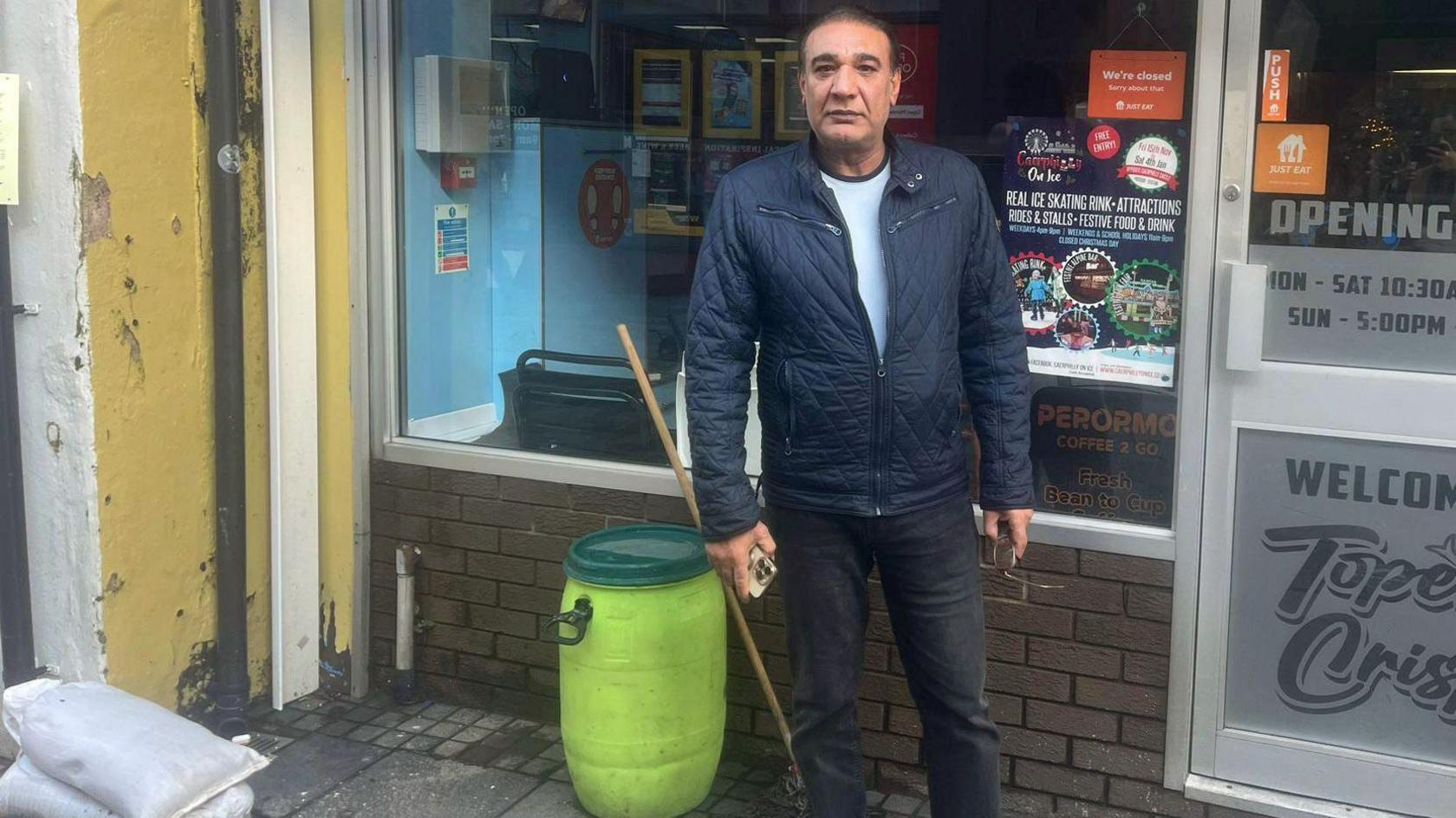 Abdul Chowdry stood outside his chip shop, with brushes and buckets in the background