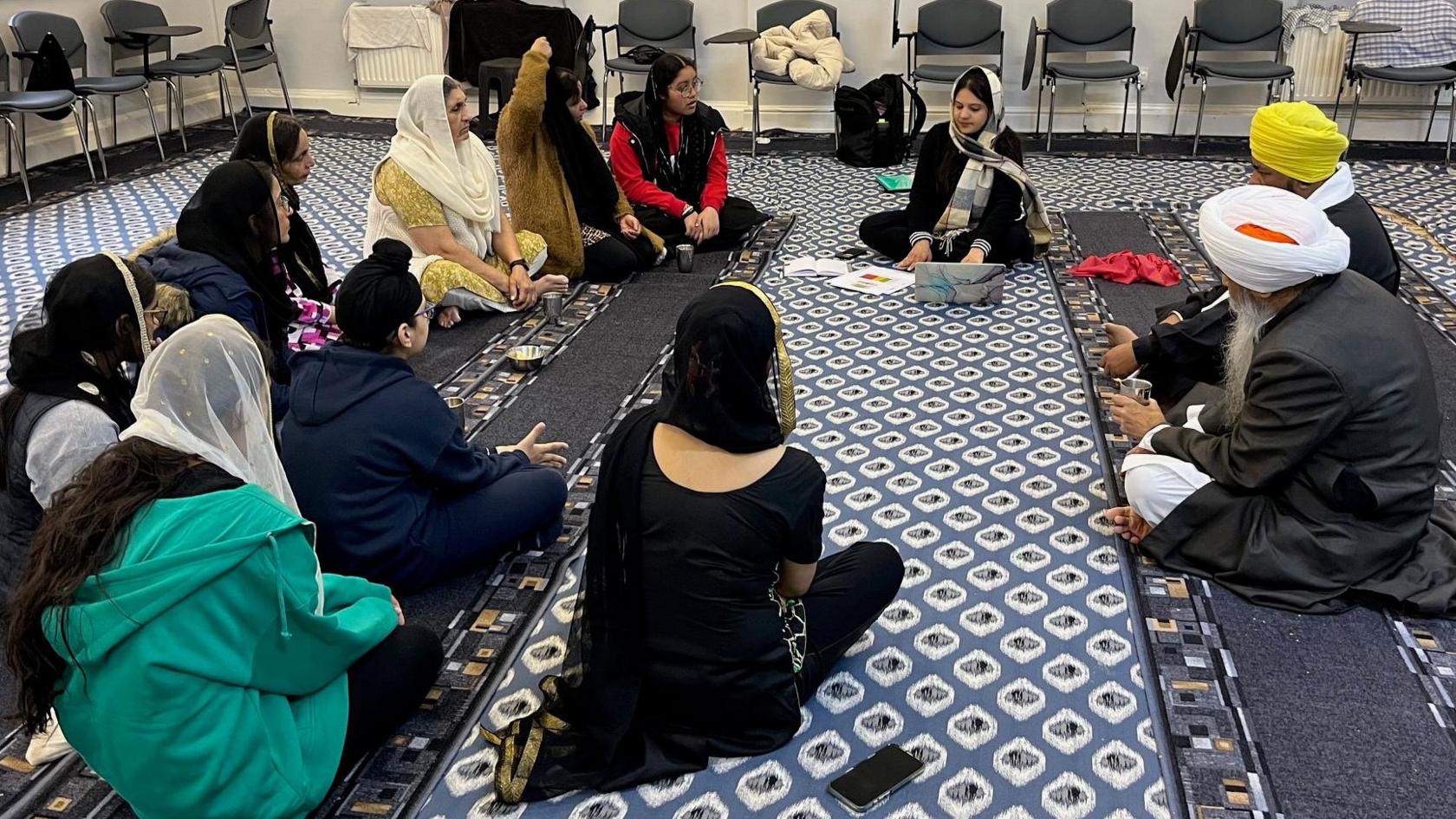 A group of people sit in a circle at a gurdwara