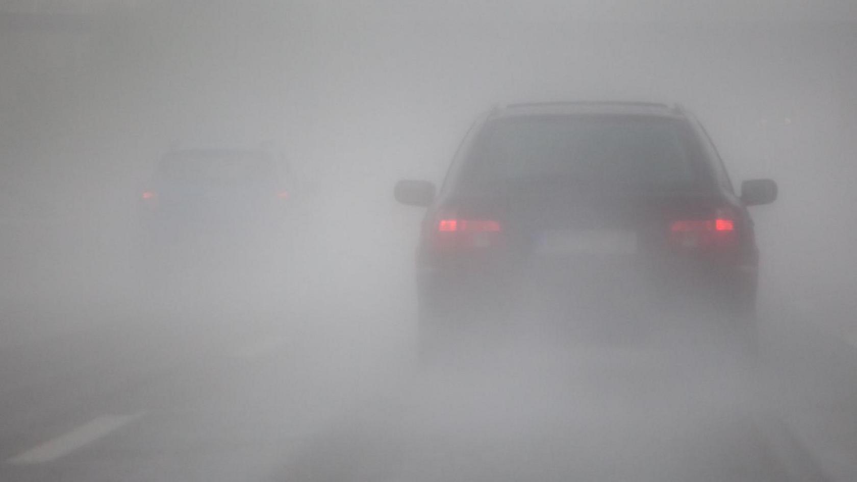 A picture of a car in reduced visibility with red brake lights on