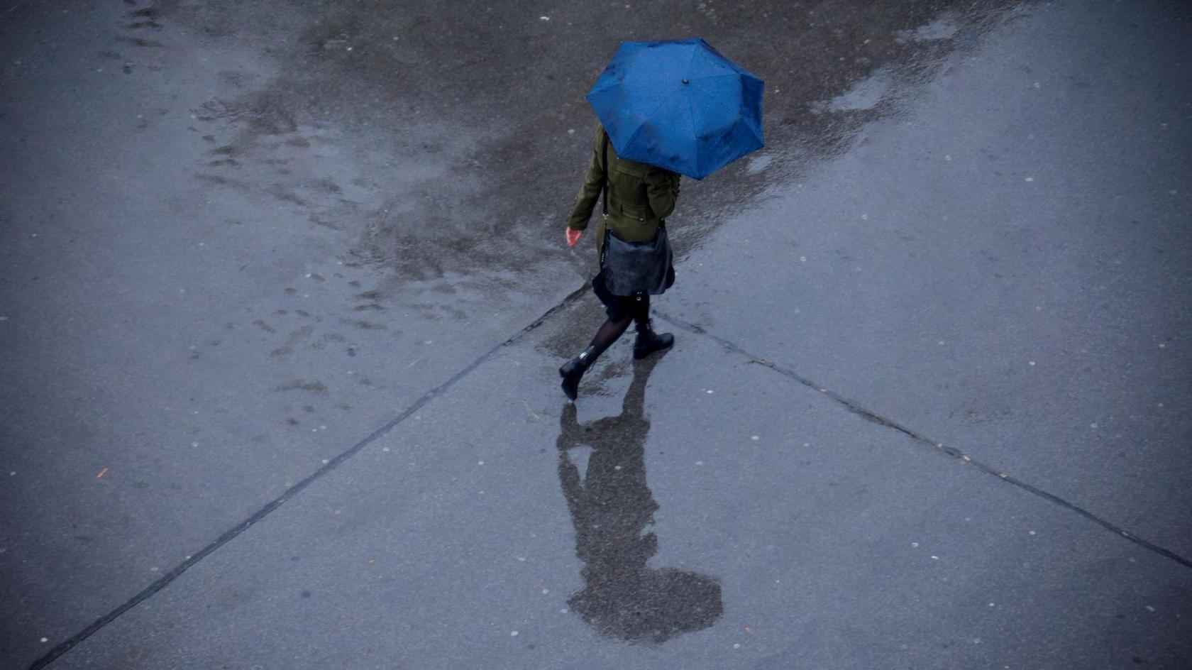 A person walking in the rain holding a blue umbrella