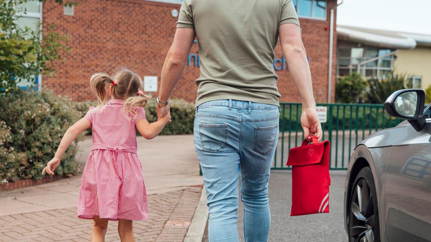 A stock image of a father holding hands with his daughter in school uniform