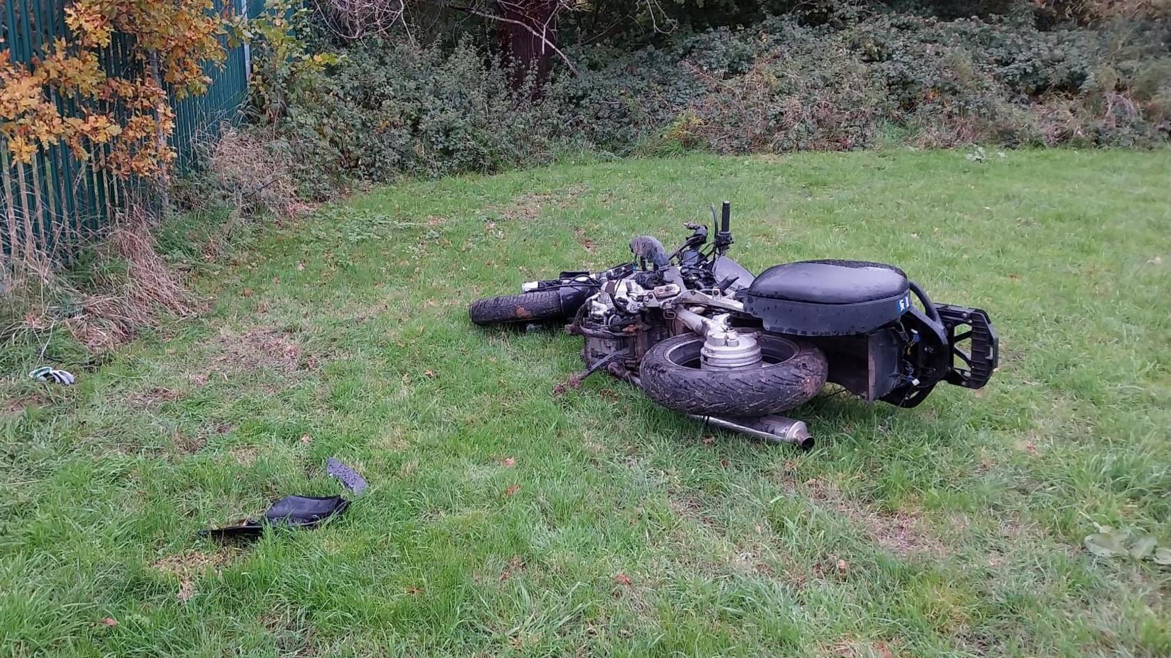 A motorbike on its side in a field, with a piece of debris which has seemingly from the bike lying nearby.