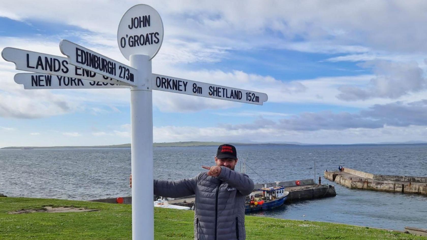 A man standing at the John O'Groats sign