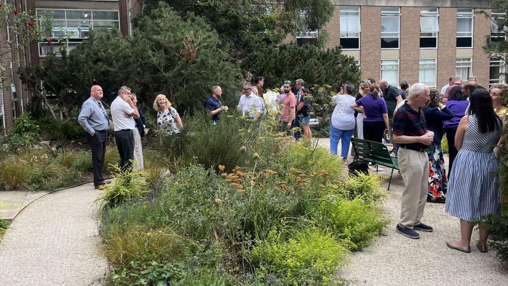 Crowd of people stand among trees and plants in Chapel Allerton Hospital's new garden