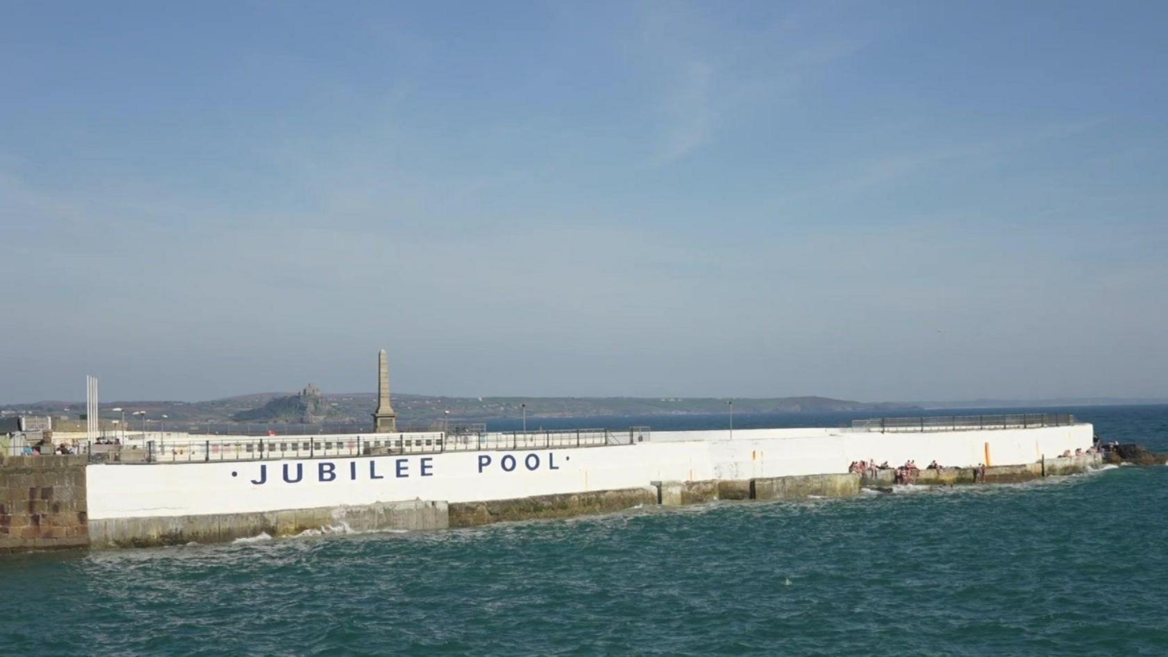 The Jubilee Pool from the outside. There is a white wall surrounding the pool and there is sea around it.