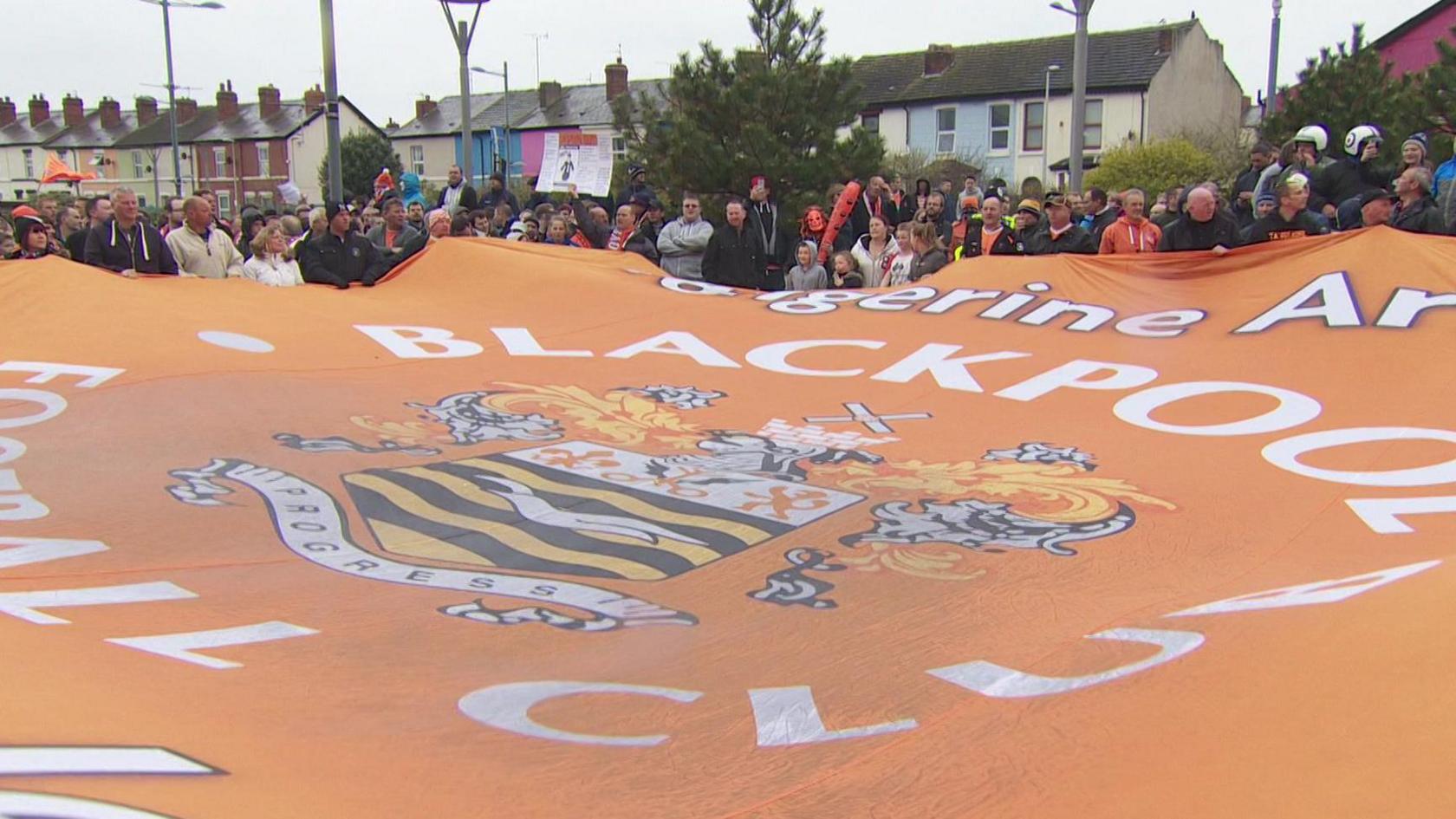 Protesting fans hold up a giant Blackpool club flag near the club's Bloomfield Road ground